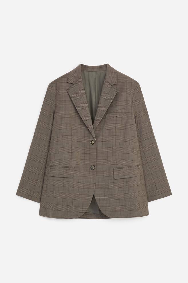 Um blazer castanho aos quadrados estÃ¡ virado para a frente, exibindo uma silhueta estruturada com lapelas de entalhe, fecho frontal de dois botÃµes e um subtil padrÃ£o glen check. O blazer apresenta um bolso de peito embutido no lado esquerdo e dois bolsos frontais com aba. - 1