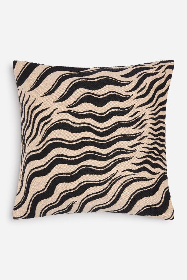A square cushion cover is shown front-on, featuring a textured jacquard-woven zebra pattern with wavy black stripes on a beige background. - 1
