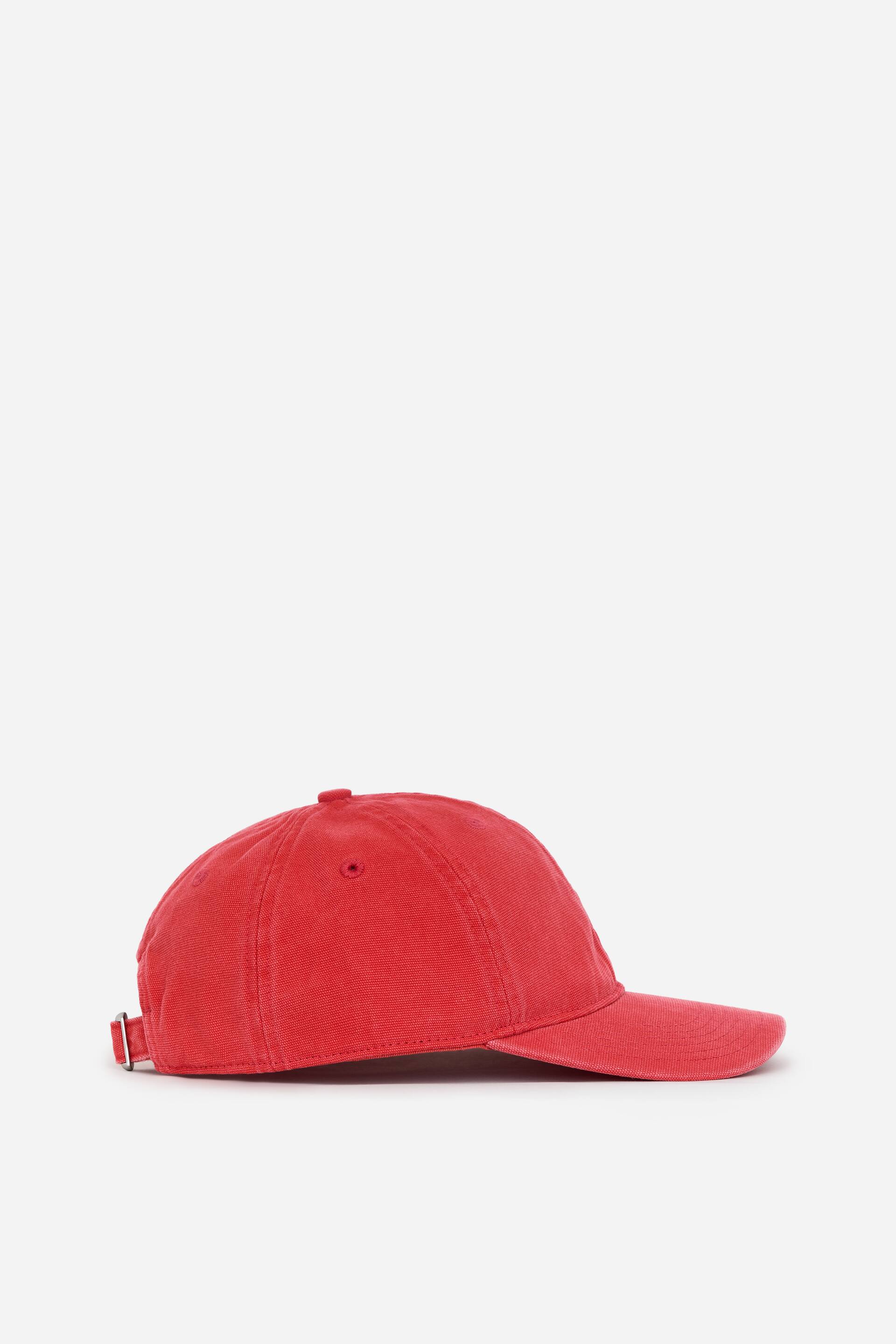 View larger image: A washed red baseball cap is presented in a side view, featuring a rounded crown and a curved brim. It displays a ventilation eyelet on the side and an adjustable strap with a silver-toned metal buckle at the back.