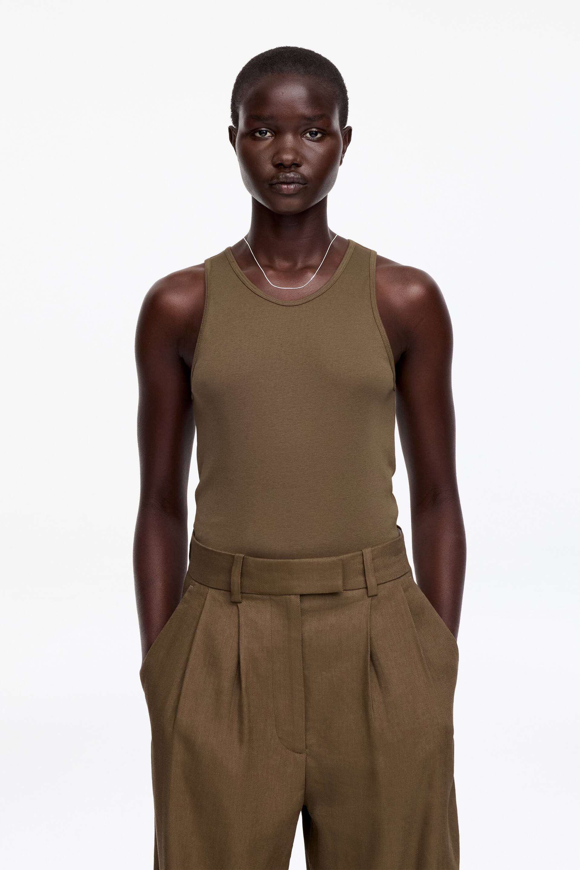 View larger image: An olive green ribbed vest top is displayed from the front, tucked into matching high-waisted pleated trousers that feature belt loops and visible side pockets.