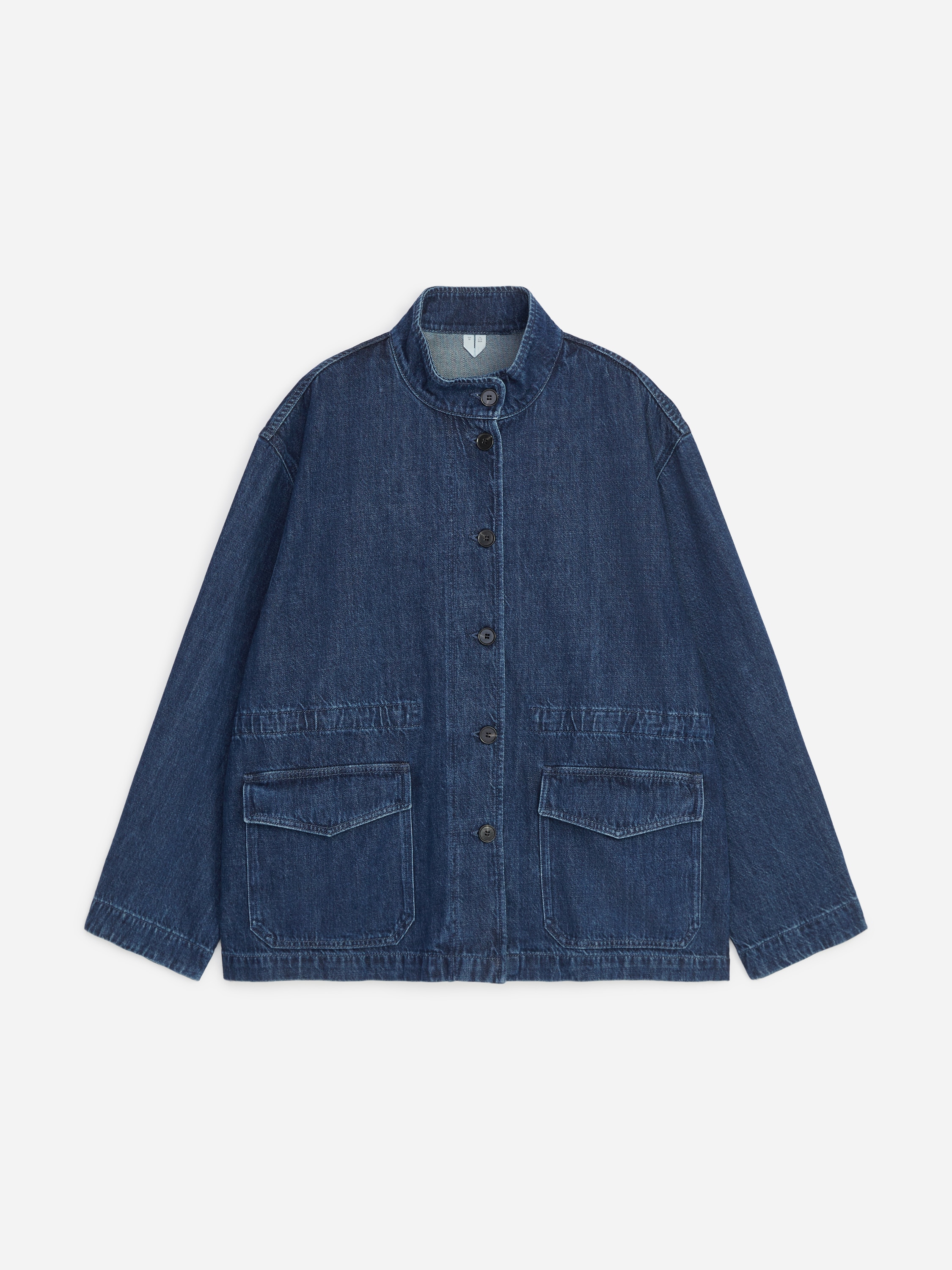 Une surchemise en denim bleu foncÃ©, dotÃ©e dâun col montant, dâune fermeture boutonnÃ©e sur le devant, dâune taille froncÃ©e et de grandes poches Ã  rabat, est portÃ©e par le mannequin. La surchemise est superposÃ©e Ã  un col roulÃ© sombre et associÃ©e Ã  un pantalon noir Ã  jambes larges.