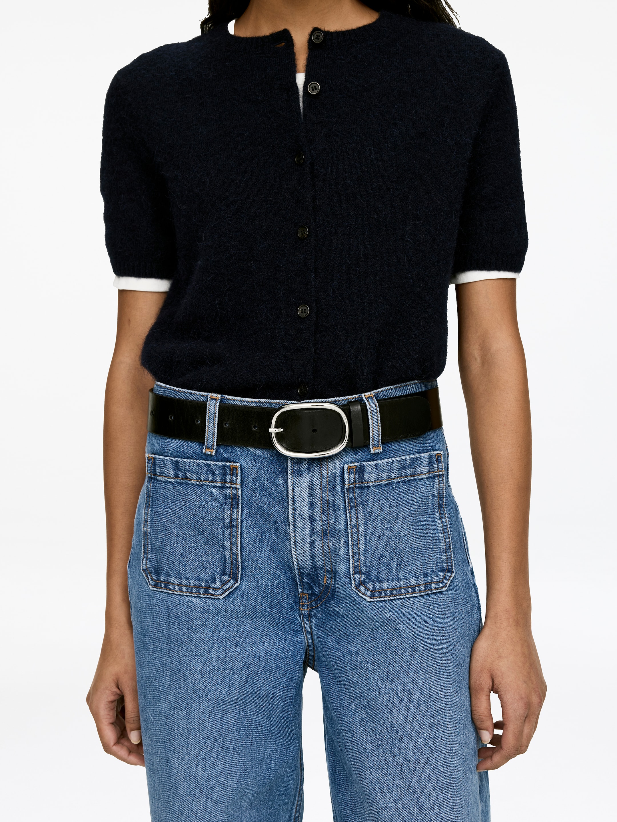 Visa större bild: Den LUPINE ljusblå stretchjeansen bärs av modellen och har en hög midja och stora fickor framtill. Ett svart bälte med ovalt spänne bärs genom jeansens hällor, som drar in midjan.