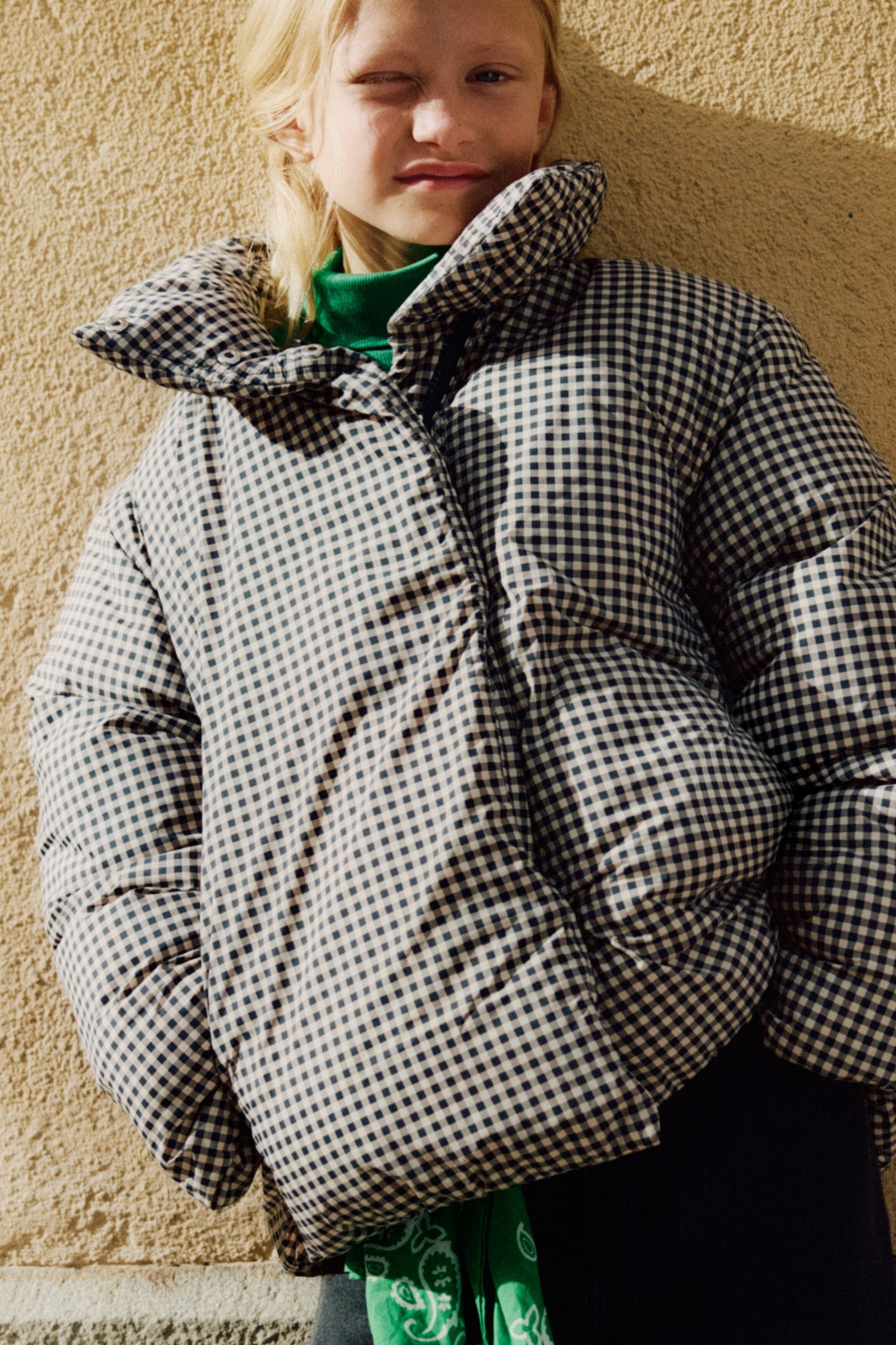 Größeres Bild ansehen: Eine Pufferjacke mit Vichy-Karomuster wird von vorne getragen und verfügt über einen hohen Kragen, eine verdeckte Frontleiste und Nahttaschen an den Seiten. Die gesteppte Oversized-Jacke wird über einem grünen Rollkragenpullover kombiniert.