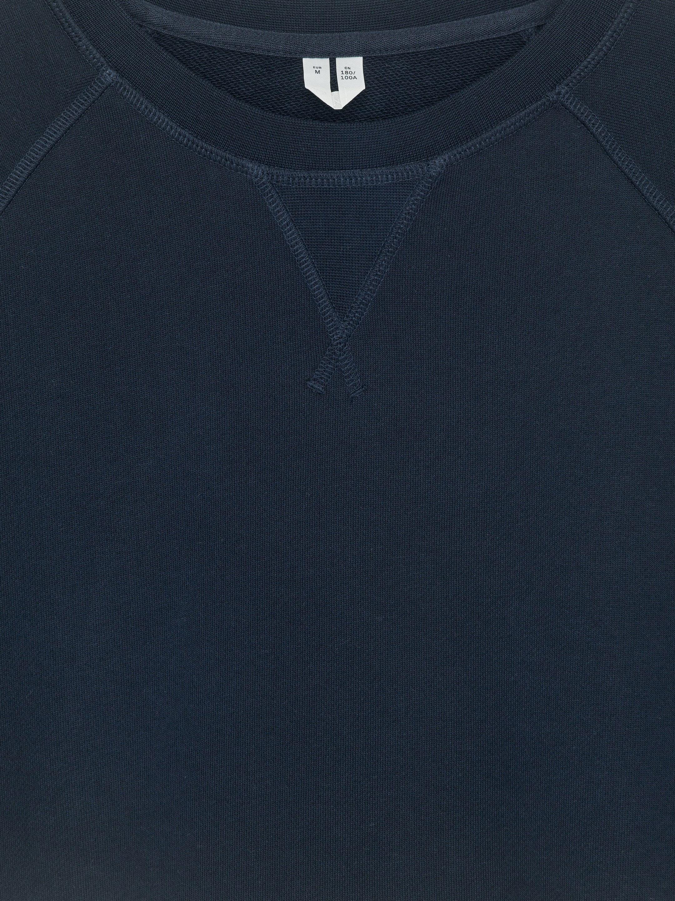 Größeres Bild anzeigen: Ein dunkelblaues Sweatshirt mit Rundhalsausschnitt wird von vorne gezeigt, mit Raglan-Ärmeln und einem gerippten Kragen. Ein V-förmiges Stichdetail ist unter dem Halsausschnitt sichtbar.