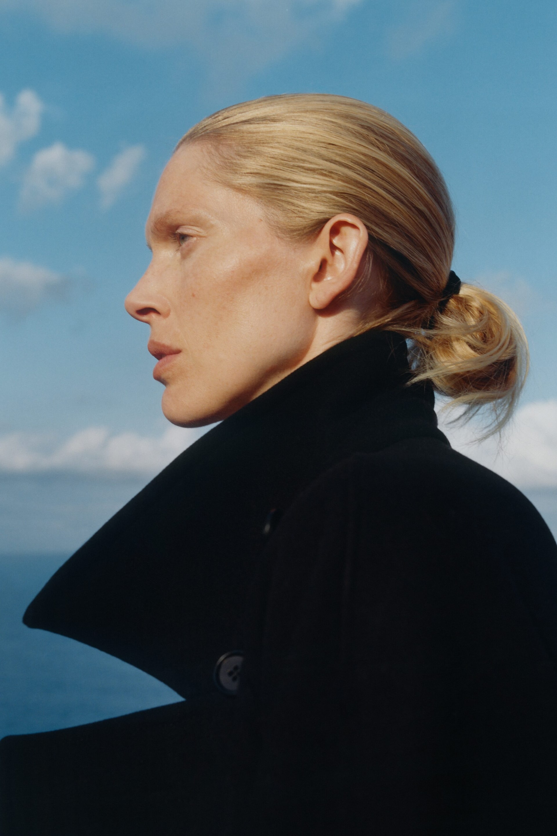 View larger image: A black coat features a wide, structured collar that stands up, with a single button visible on the lapel area.