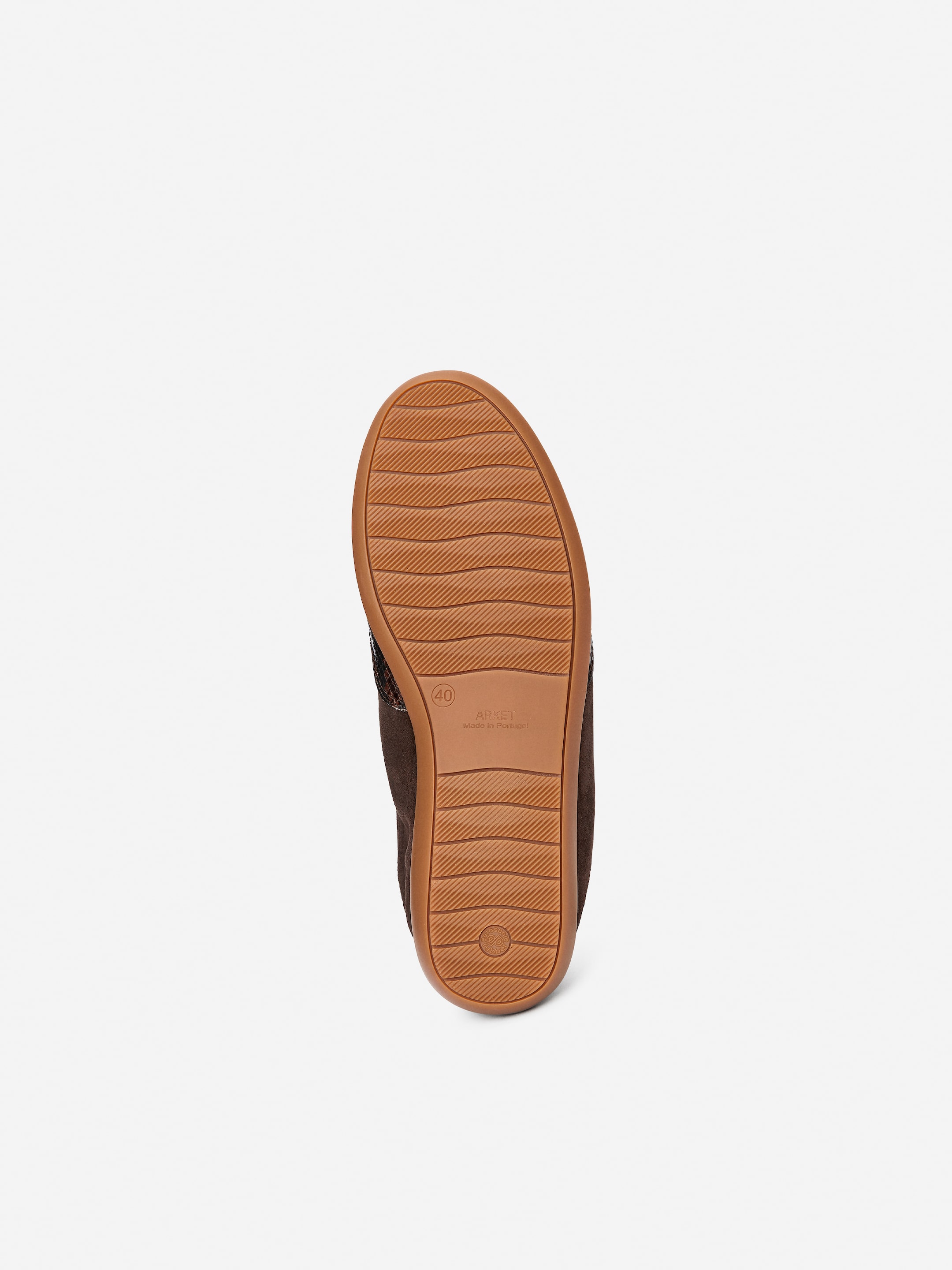 View larger image: A dark brown trainer is being presented from a bottom angle, revealing its textured, reddish-brown sole. The sole is featuring wavy grip patterns and embossed product information.