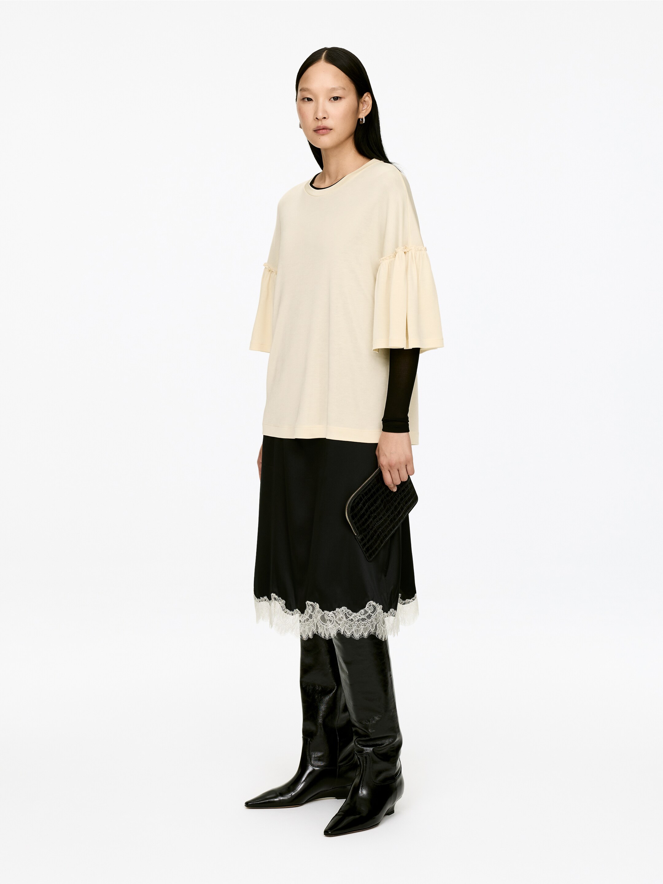 Visa större bild: En krämfärgad T-shirt med rund hals och volangärmar i vanlig passform bärs av modellen, lager på lager över en svart långärmad top.