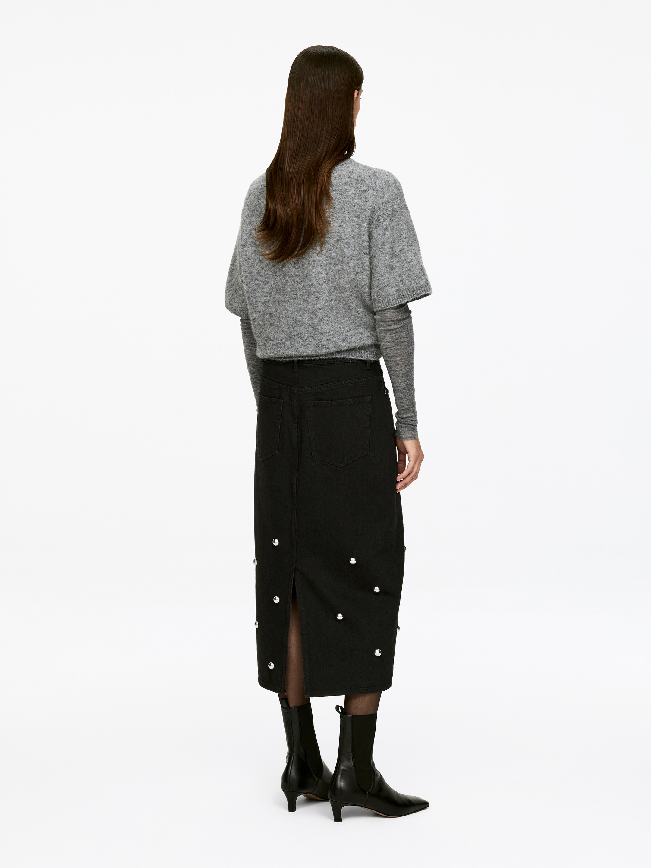 Agrandir l'image: Une jupe noire mi-longue, confectionnée en coton et dotée d'un design à cinq poches, est portée par le mannequin. La jupe à la coupe régulière présente des clous dispersés et une fente à l'arrière.