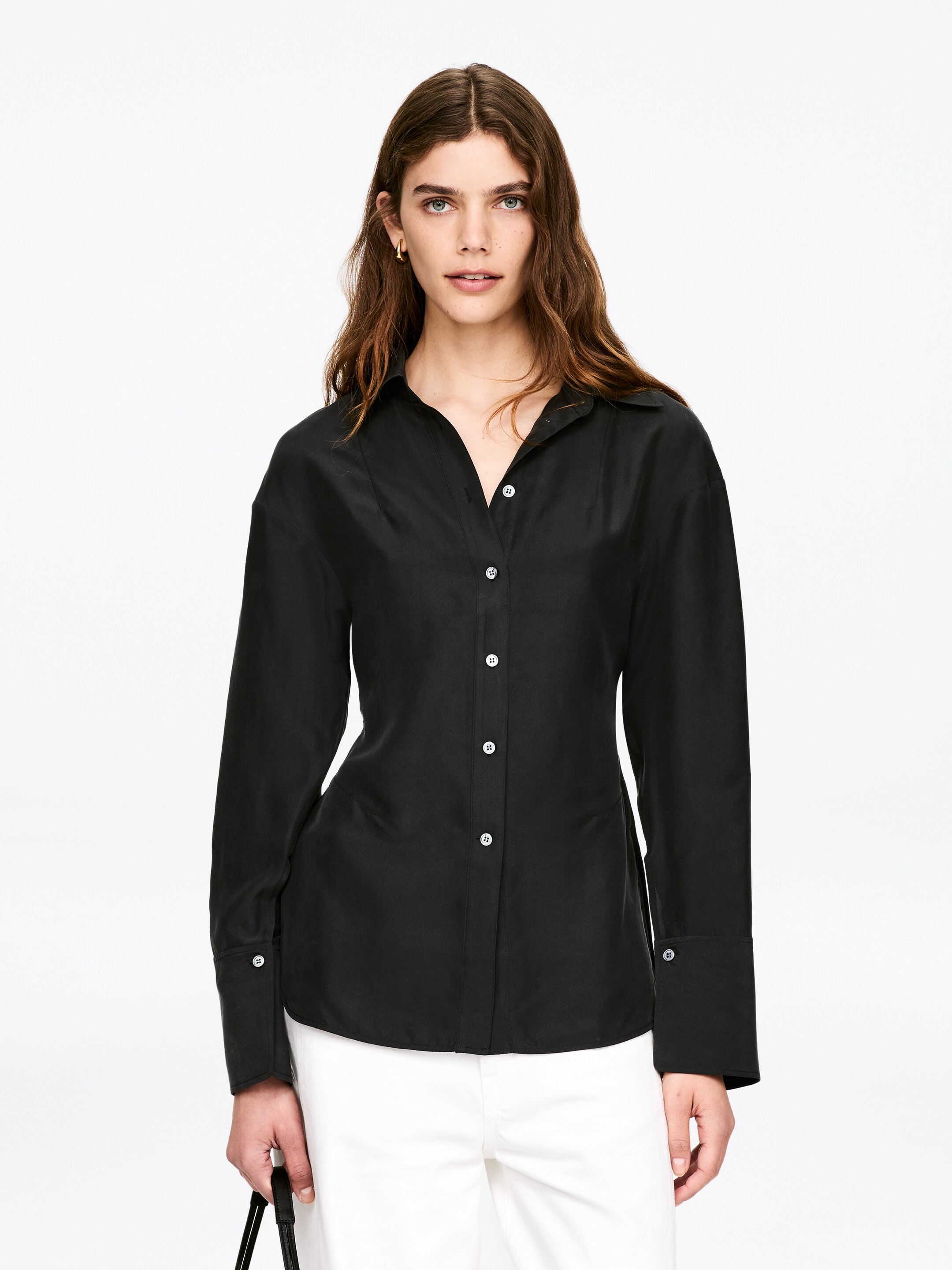 Преглед на по-голямо изображение: Черен риза с копчета отпред, с отворена яка, разкриваща V-образно деколте, и преден плакет с бели копчета. Представя дълги ръкави с широки маншети с едно копче и втален силует, като материята показва лек блясък.