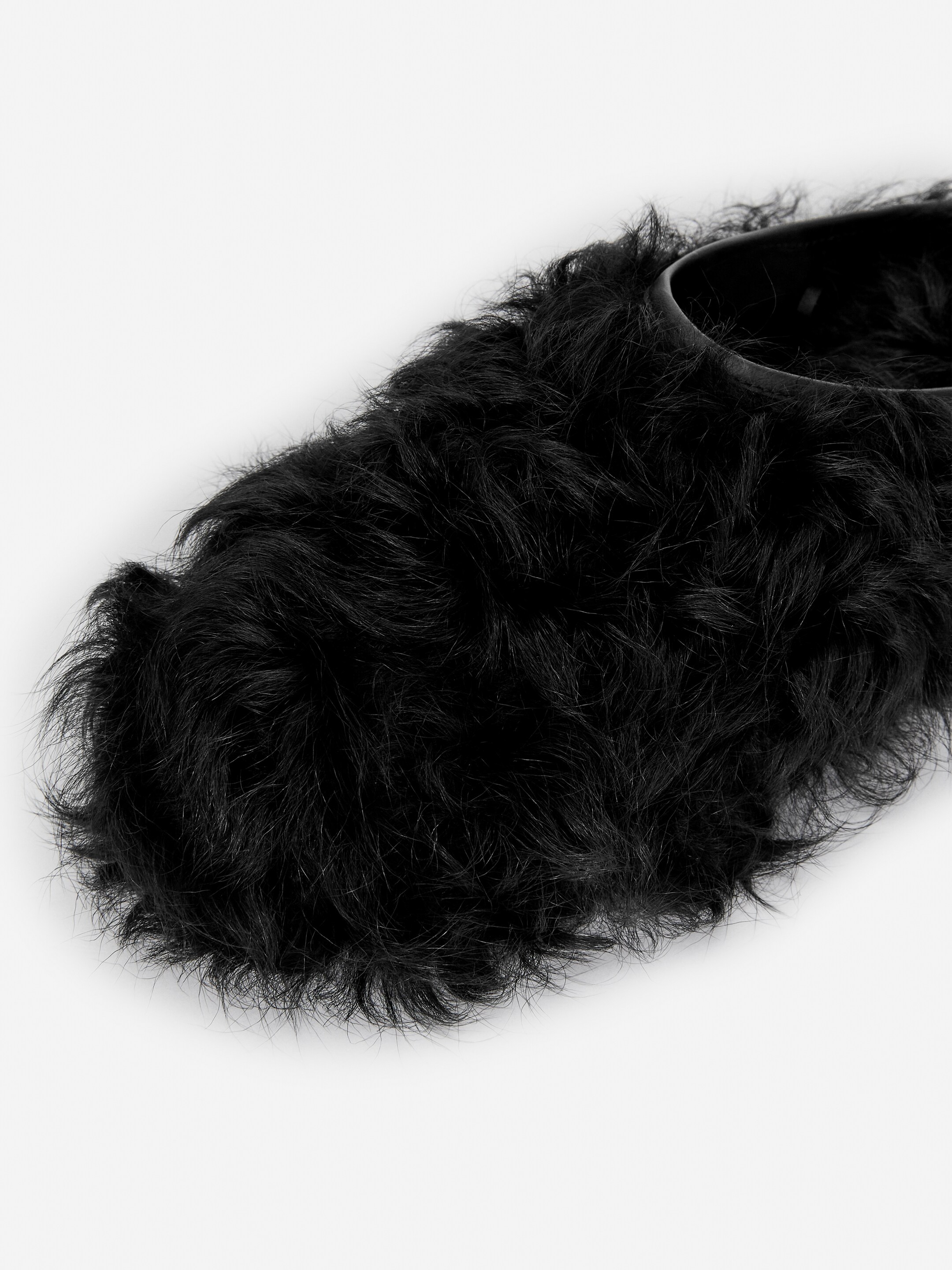 Agrandir l'image: Une pantoufle en fourrure noire à poils longs est orientée vers la droite, sa partie supérieure recouverte d'une texture hirsute, avec un col lisse et sombre visible autour de l'ouverture pour le pied.