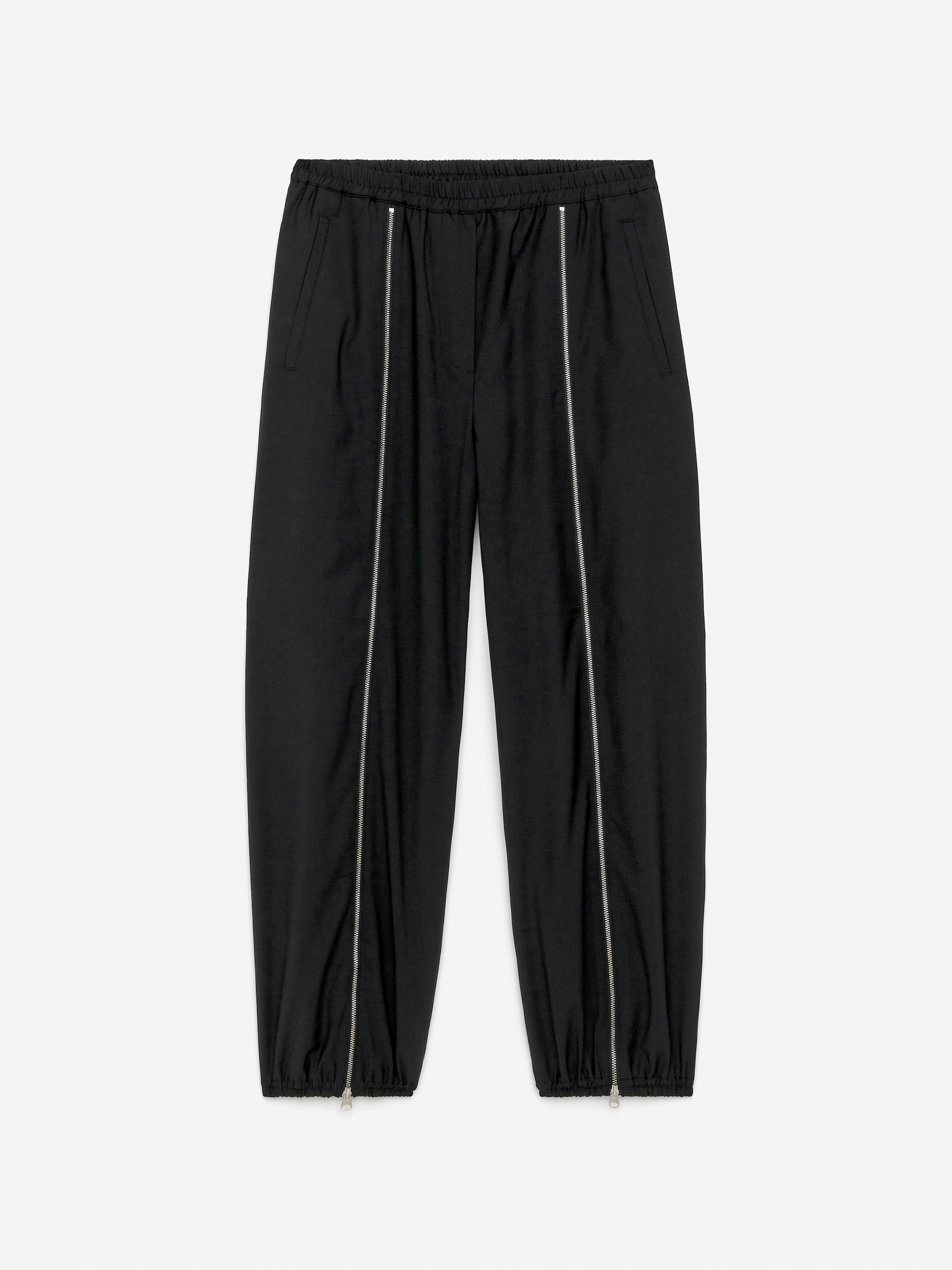 Visualizza immagine più grande: I pantaloni della tuta neri sono presentati dalla parte anteriore, con una vita e polsini elasticizzati. Dettagli con zip verticali in tonalità argento corrono lungo ciascuna gamba, completando la silhouette affusolata e le tasche laterali a filetto visibili.