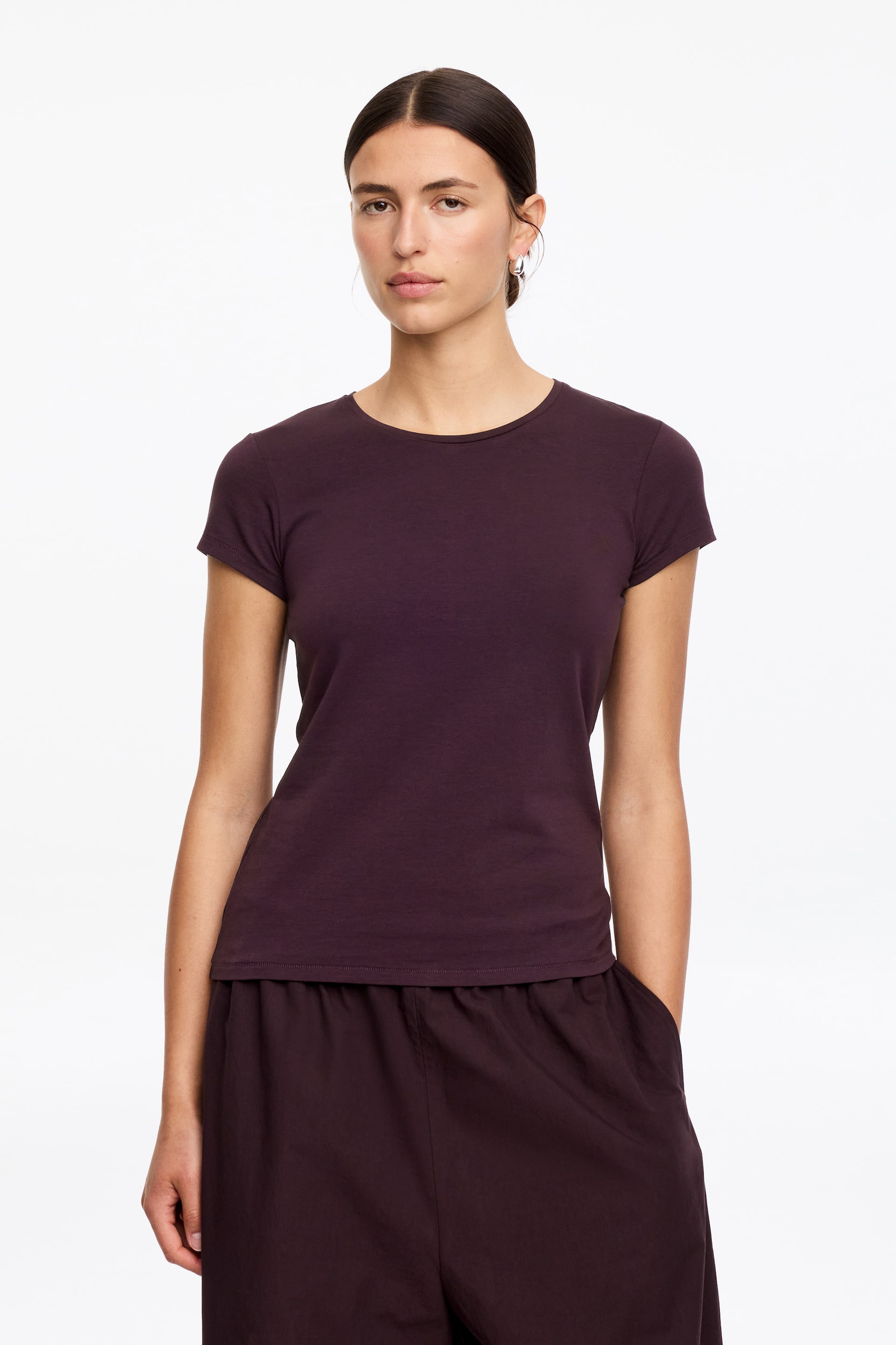 Agrandir l'image: Le modèle porte un T-shirt ajusté de couleur prune foncée. Il présente un col rond et des manches courtes, formant une silhouette cintrée.