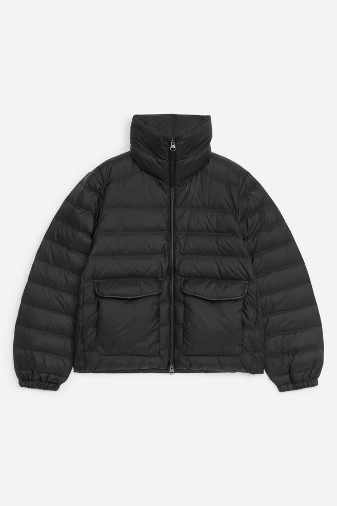 La giacca imbottita Re:Down Ã¨ mostrata frontalmente, con un design nero trapuntato orizzontalmente, colletto alto rialzato e zip frontale a tutta lunghezza. Presenta due ampie tasche applicate frontali con patta e polsini elasticizzati sulle maniche. - 1