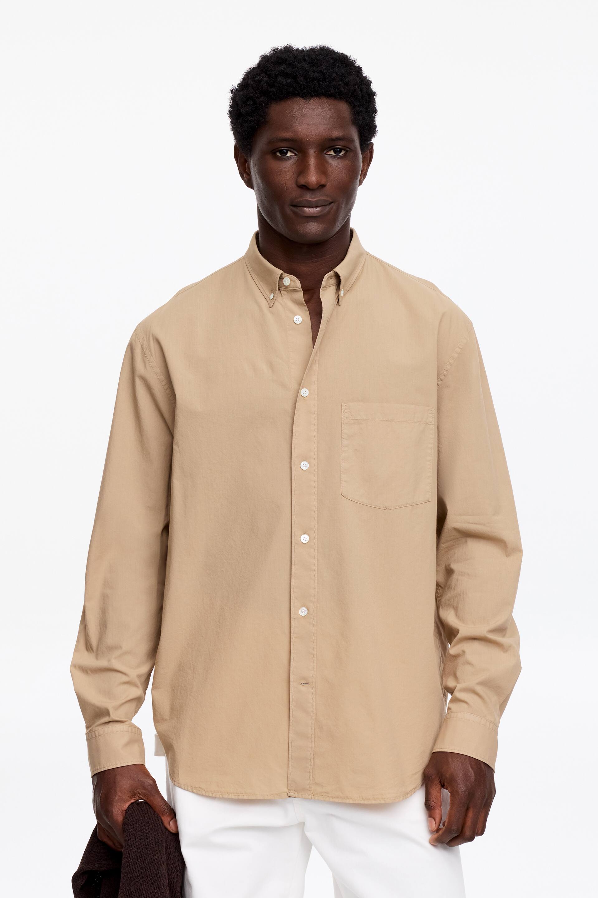 Zobrazit větší obrázek: Béžová košile s dlouhým rukávem je otočená dopředu, ukazuje límec na knoflíky a celou řadu knoflíků s bílými knoflíky. Má jednu náprsní kapsu na levé straně a manžety na knoflíky.