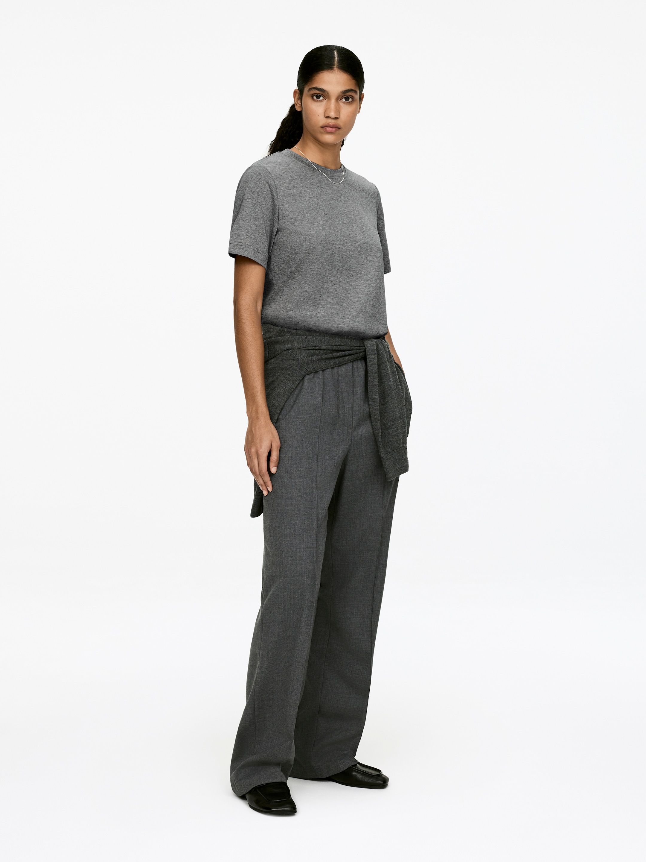 View larger image: A grey crew neck T-shirt, featuring short, softly tailored sleeves and a regular fit, is being worn by the model. A matching grey sweater is tied around the model's waist, layered over the T-shirt.