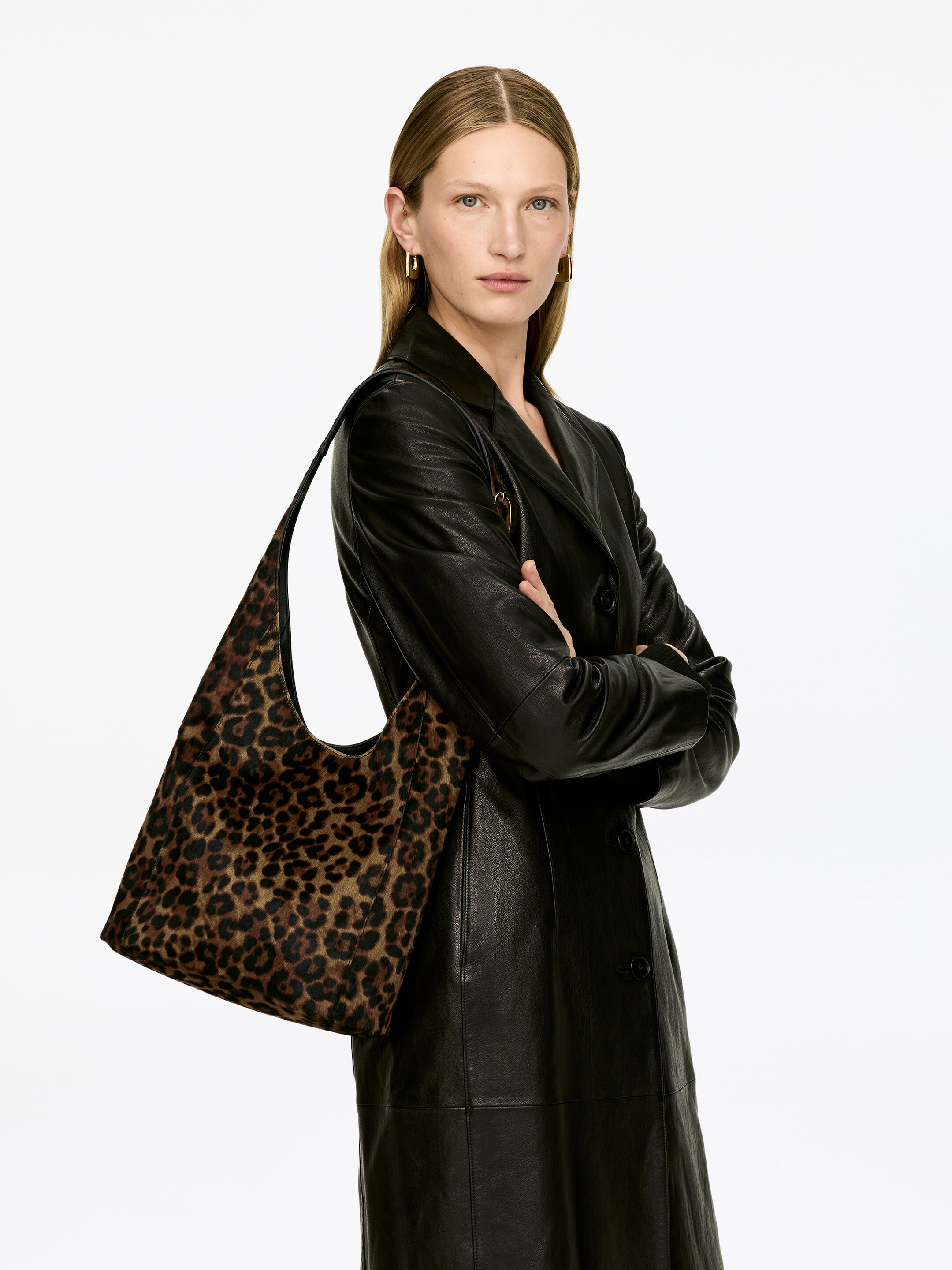 Grotere afbeelding bekijken: Een hobo tas met luipaardprint wordt over een schouder gedragen, hangend met een zachte, ongestructureerde val. Het heeft een patroon van bruine en zwarte vlekken op een lichtbruine achtergrond, zichtbaar vanuit een licht schuine vooraanzicht.