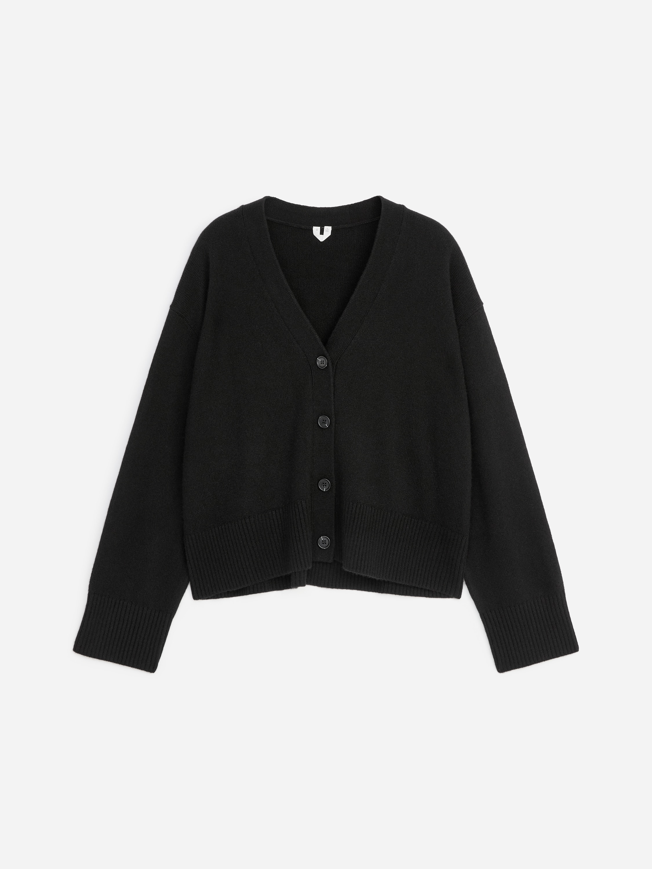 La modella indossa un cardigan nero in cashmere con scollo a V profondo, chiusura frontale con bottoni e finiture a coste su polsini e orlo. Il cardigan Ã¨ abbinato a un top bianco e a pantaloni neri.