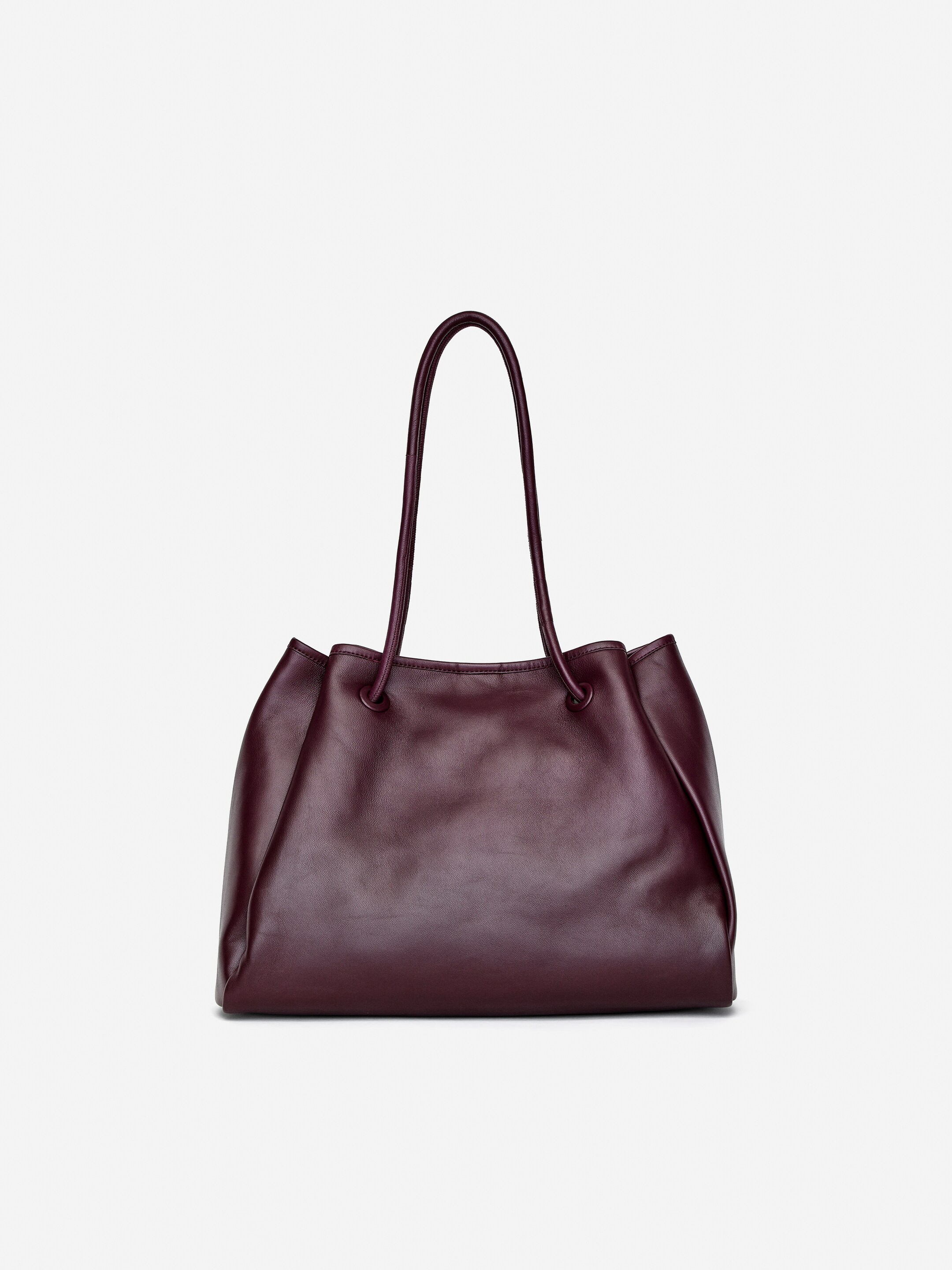 Agrandir l'image: Un sac fourre-tout en cuir bordeaux est orienté vers l'avant, avec deux poignées supérieures fines. Son corps souple se rassemble à l'ouverture supérieure, créant de subtils plis le long des côtés.