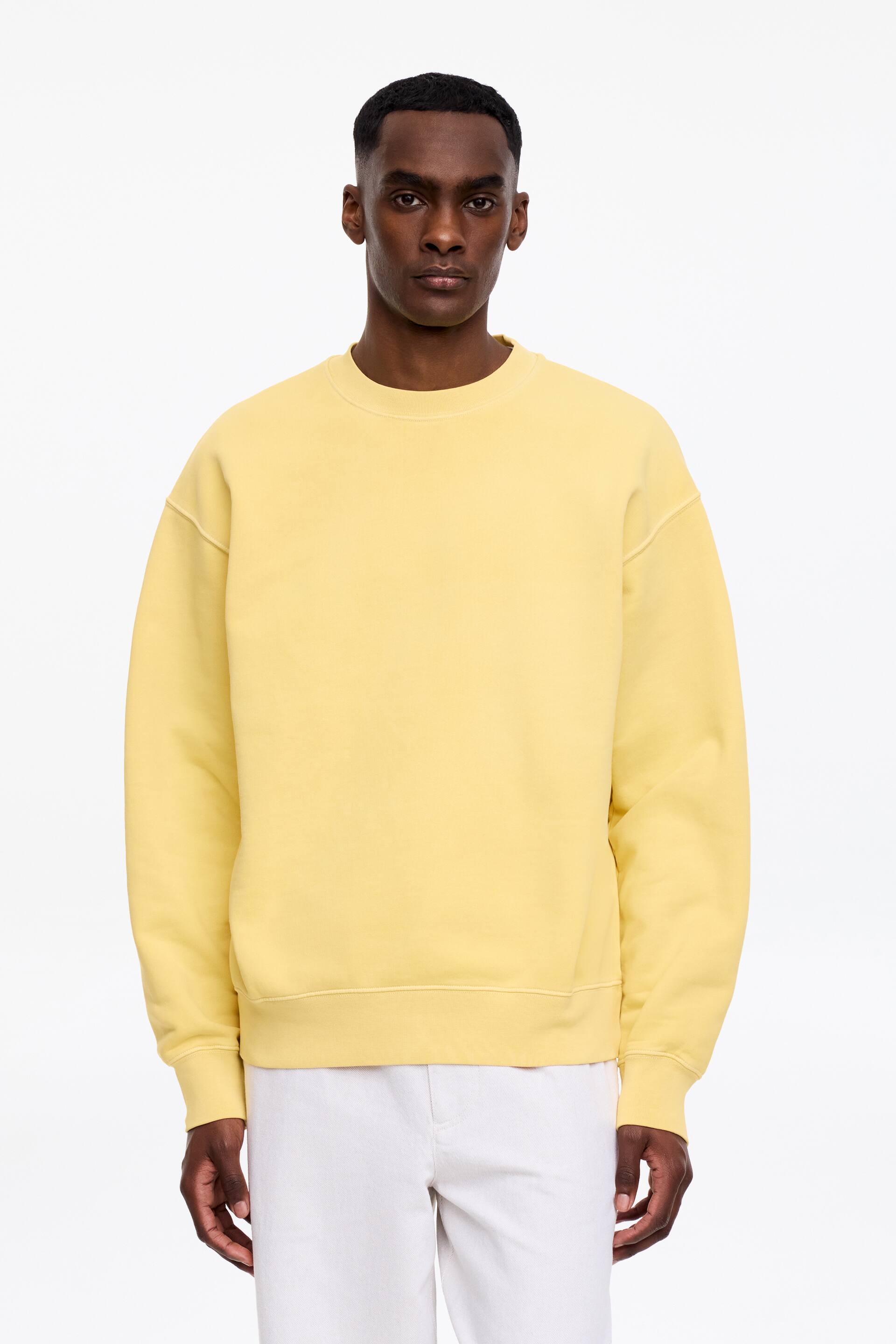 Visa större bild: Den gula tröjan med rund hals har en avslappnad passform, sedd framifrån. Den visar upp ribbade muddar, en ribbad fåll och en ribbad krage, med synliga sömdetaljer längs ärmhålen och sidsömmarna.