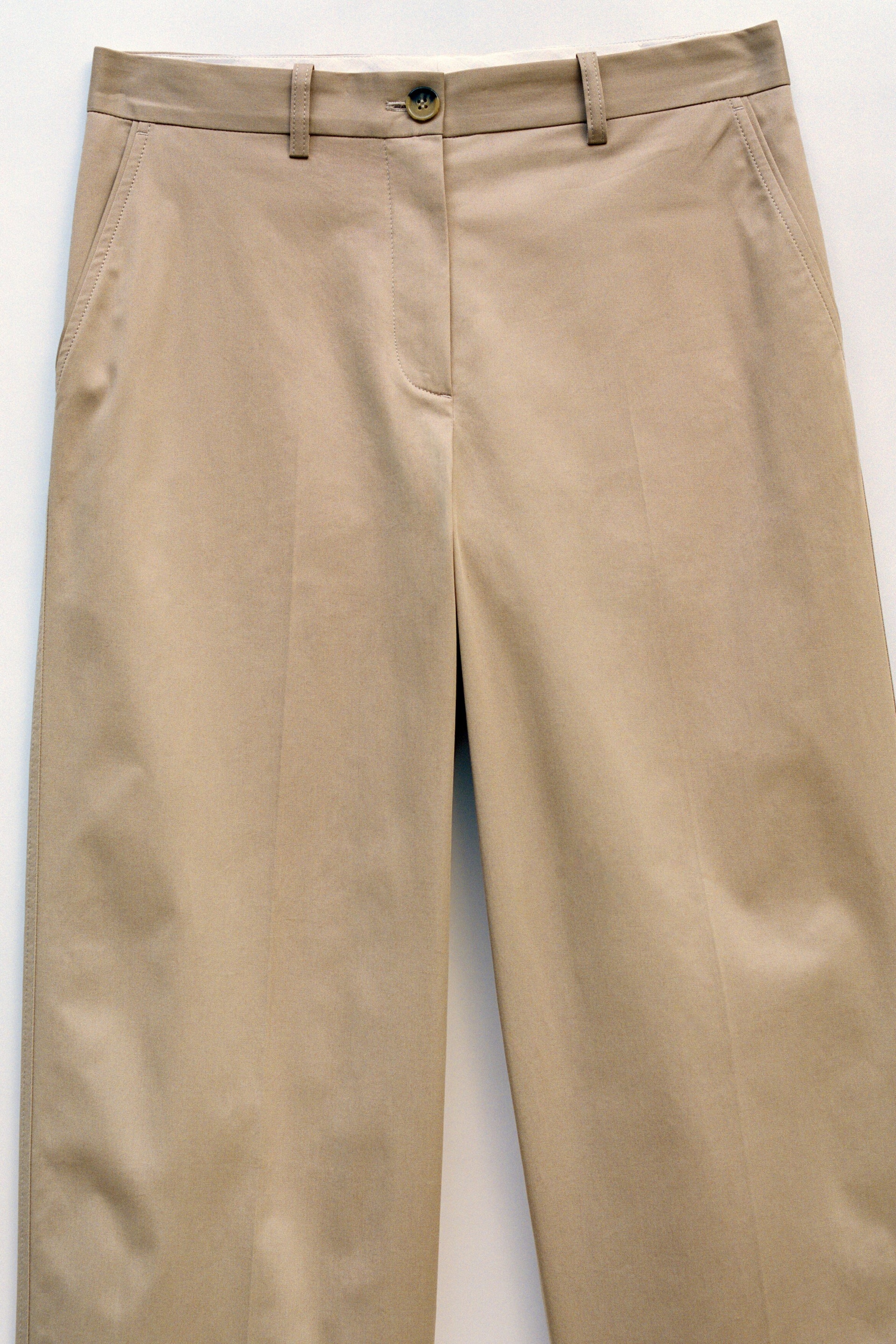 Grösseres Bild ansehen: Khakifarbene Wide-Leg-Hose liegt flach und nach vorne ausgerichtet, mit einem flachen Bund mit Gürtelschlaufen, einem einzelnen Knopfverschluss, schrägen Seitentaschen und dezenten Bügelfalten, die vorne an jedem Hosenbein nach unten verlaufen.