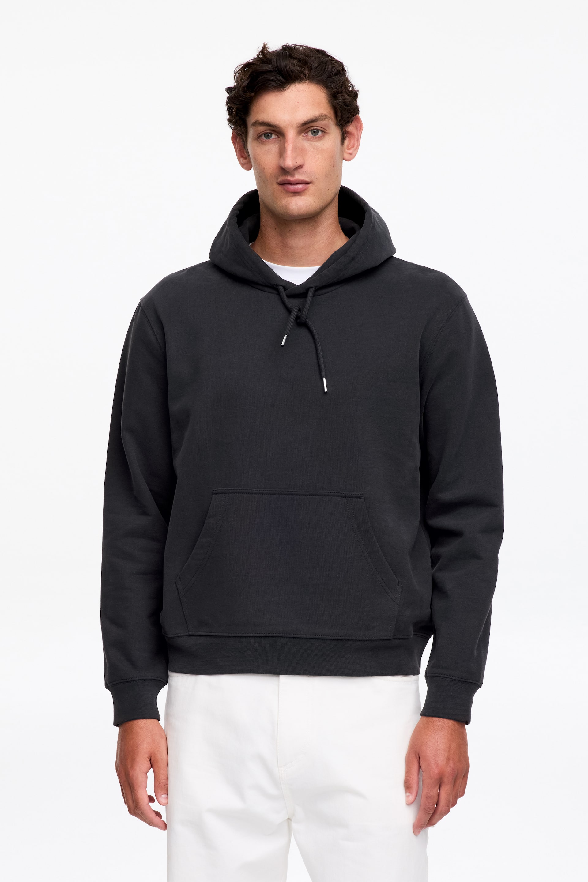 Visualizza immagine più grande: Una felpa con cappuccio grigio scuro viene presentata frontalmente. Presenta un cappuccio con laccetti bianchi, una tasca a marsupio, polsini a coste e un orlo a coste, con una t-shirt bianca visibile allo scollo.