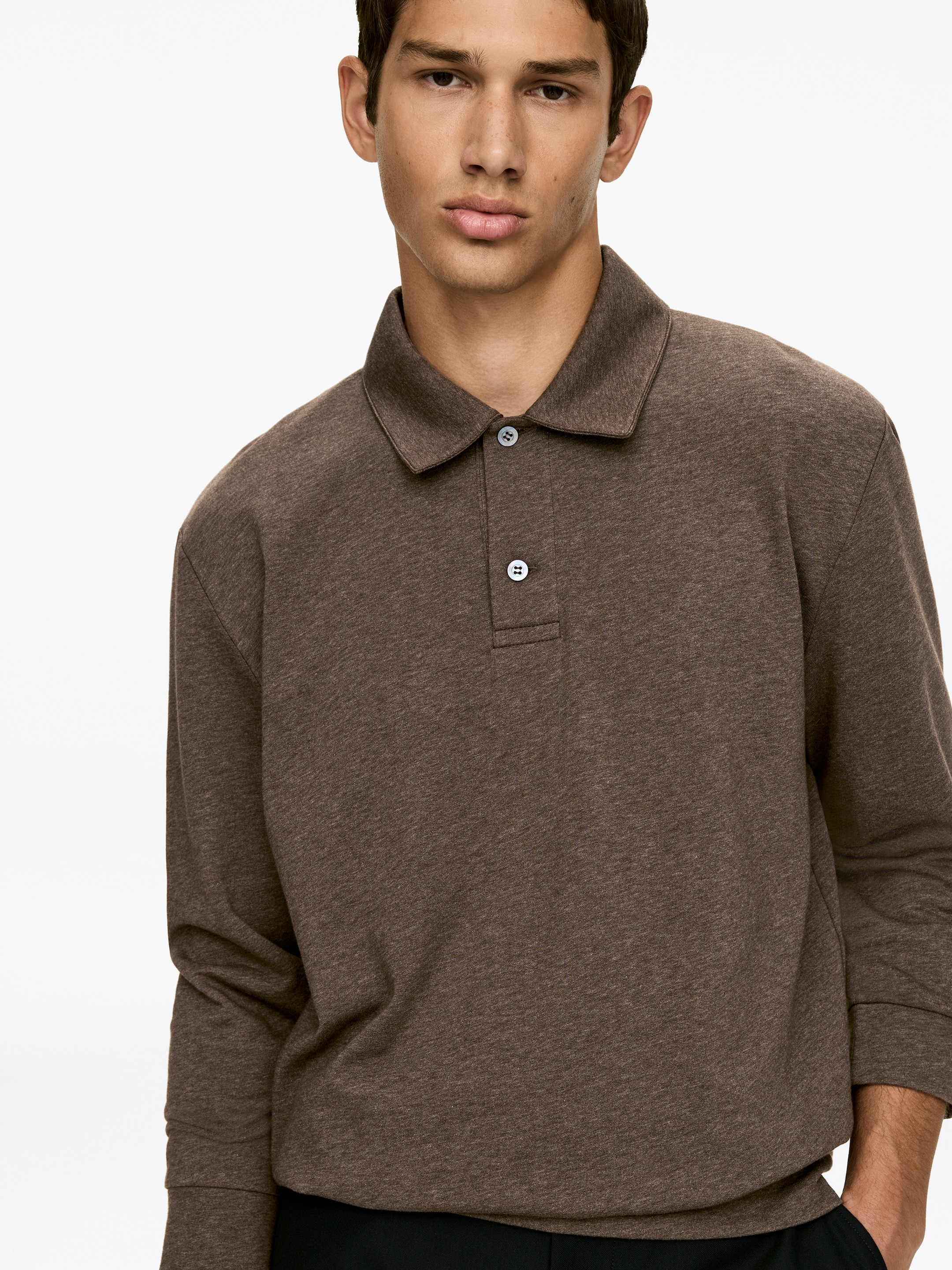 Grotere afbeelding bekijken: Een poloshirt met lange mouwen heeft een gemêleerde bruine stof en een klassieke spreidkraag. Het toont een sluiting met twee knopen met lichtgekleurde knopen en lange mouwen met eenvoudige manchetten, iets naar rechts gericht.