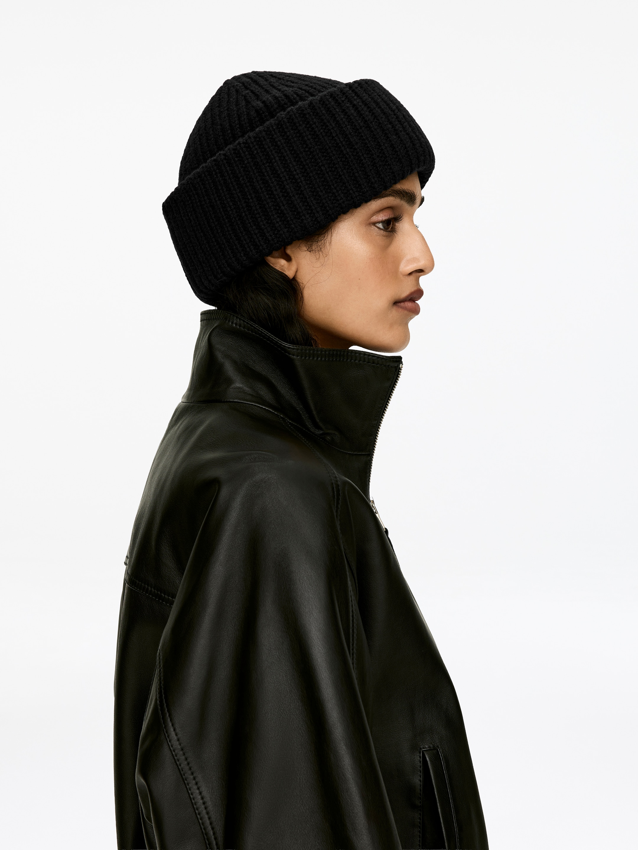 Agrandir l'image: Un bonnet noir en laine à double pli, tricoté au point arrête, est porté par le modèle. Le bonnet est assorti d'une veste en cuir noir.