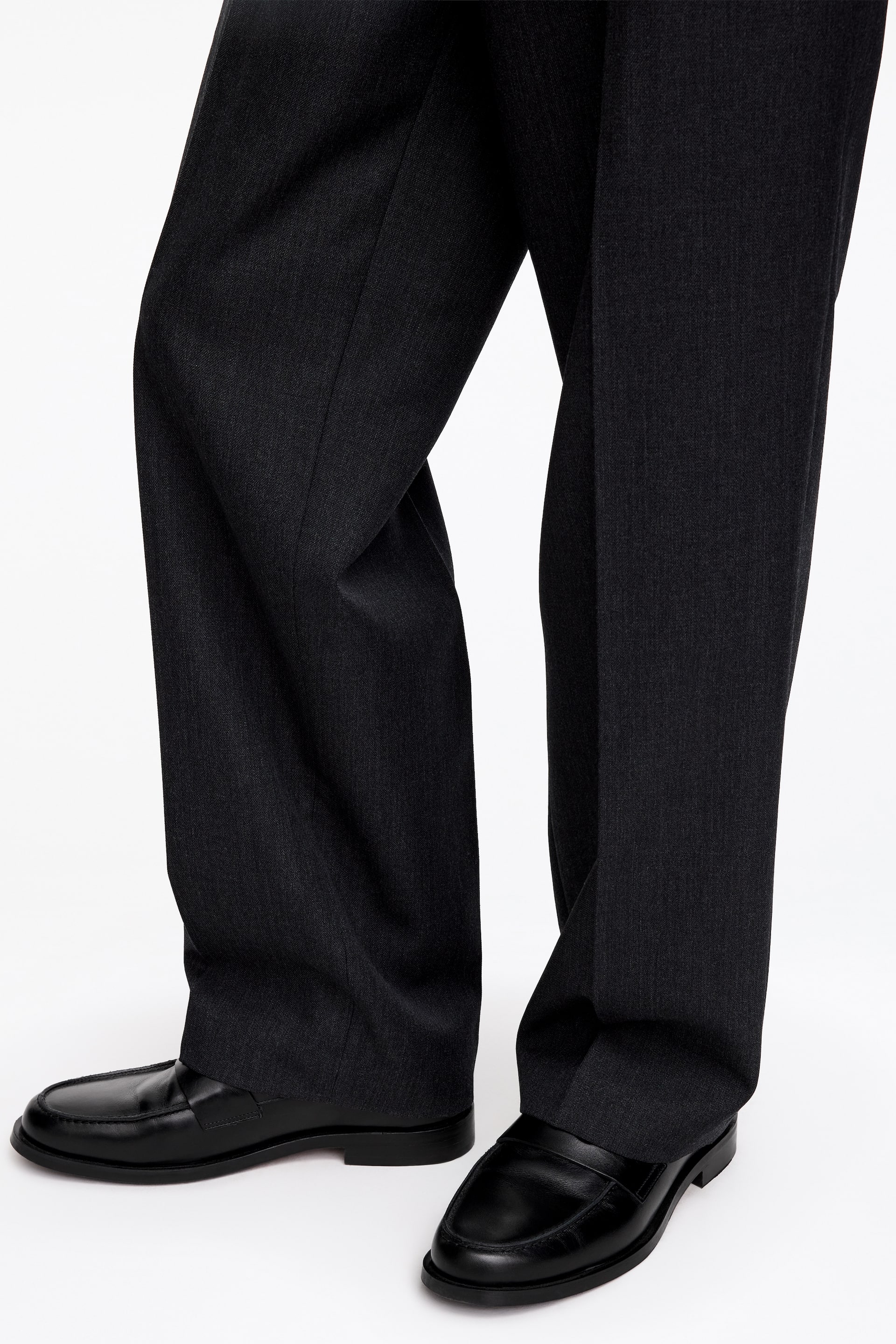 Agrandir l'image: Des mocassins en cuir noir avec une finition semi-brillante sont portés par le mannequin, associés à un pantalon foncé. Les mocassins présentent une semelle en cuir superposée et des détails de trépointe au niveau de la pointe.