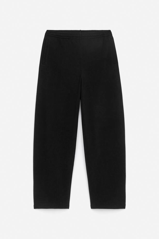 Schwarze Jogginghosen werden von vorne gezeigt, gefertigt aus einem weichen Strickstoff. Sie verfügen über einen elastischen Bund mit einem sanft gerafften Effekt, seitliche Leistentaschen und eine leicht fassförmige Beinform für eine entspannte Silhouette. - 1