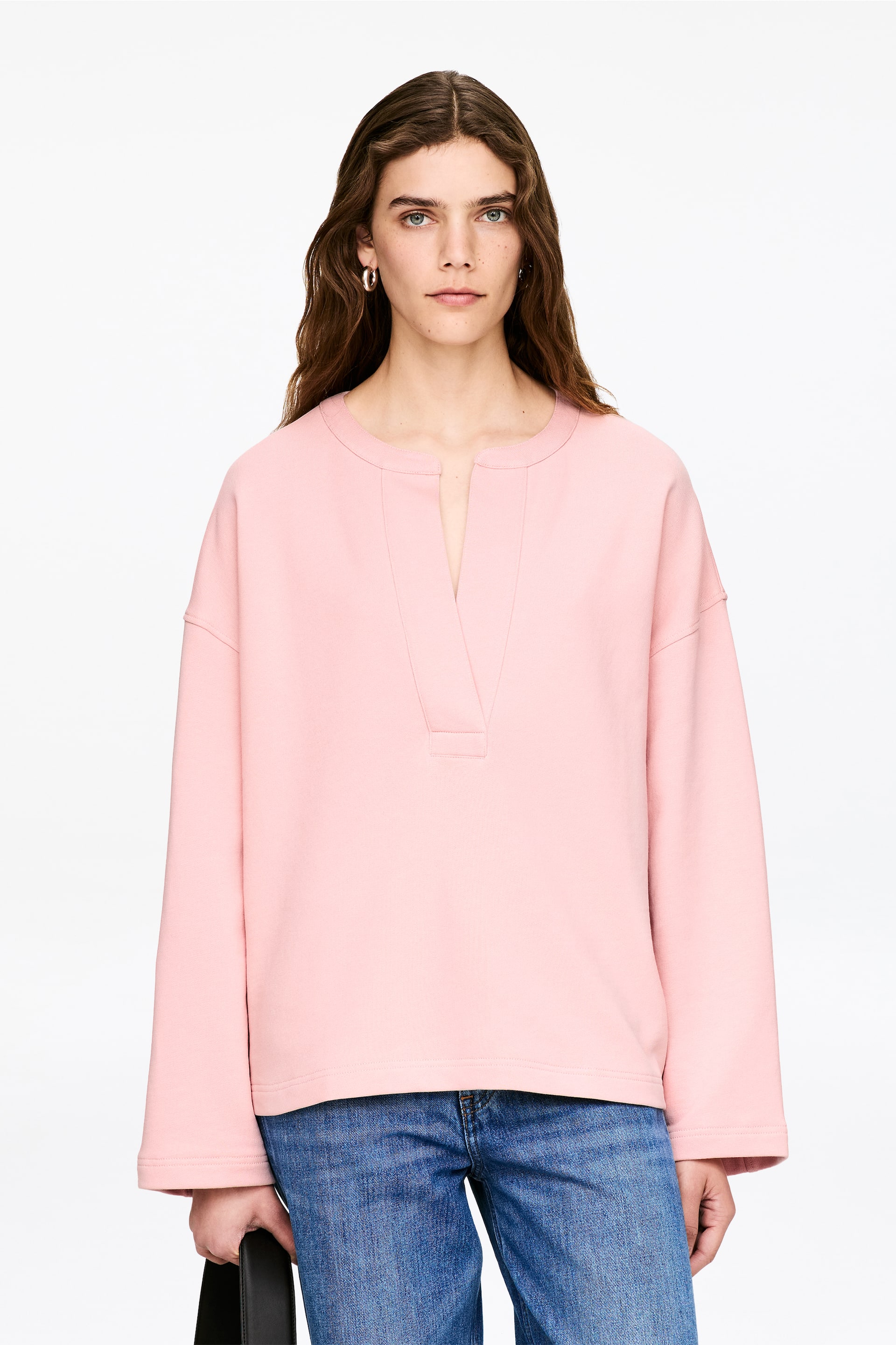 Visa större bild: En rosa pullover-topp visas framifrån, med rund halsringning och V-split placket. Den har nedhasade axlar, långa vida ärmar och en rak fåll.