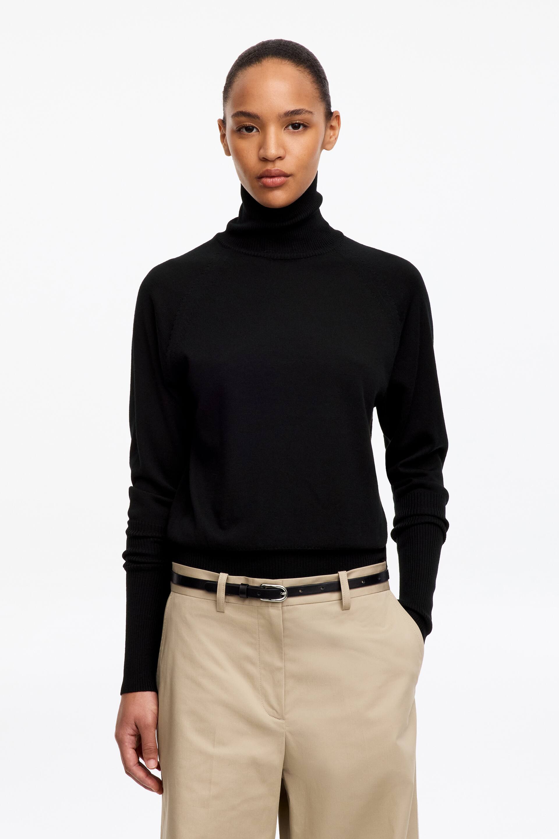 Größeres Bild ansehen: Das Model trägt einen schwarzen Rollkragenpullover. Er verfügt über einen hohen Rollkragen, gerippte Abschlüsse und verlängerte Ärmelbündchen.