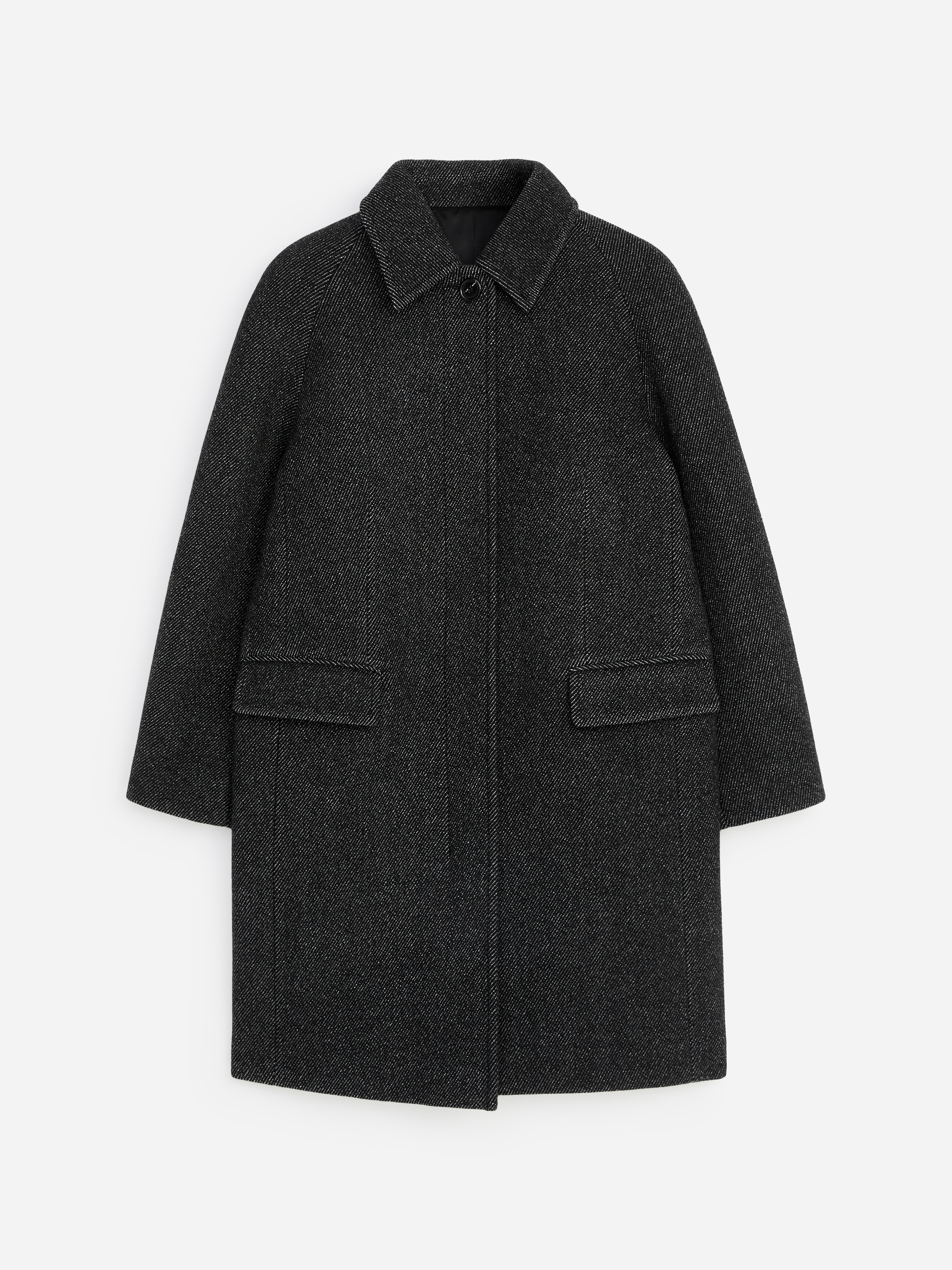 The model is wearing a dark grey, textured wool-blend coat featuring a classic collar, front flap pockets, and a knee-length hem. The coat is layered over a dark roll-neck sweater, with black over-the-knee boots and a black leather handbag carried in one hand.