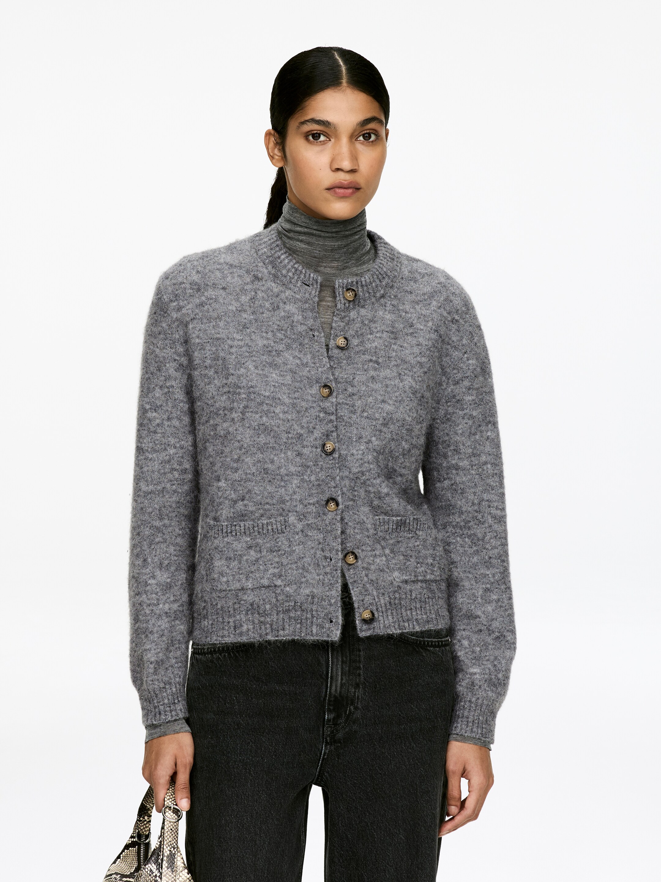Agrandir l'image: Un cardigan gris et duveteux en maille est présenté de face, stylé sur un col roulé gris. Il présente un col rond, cinq boutons bruns sur le devant, deux poches plaquées, ainsi que des poignets et un ourlet côtelés.