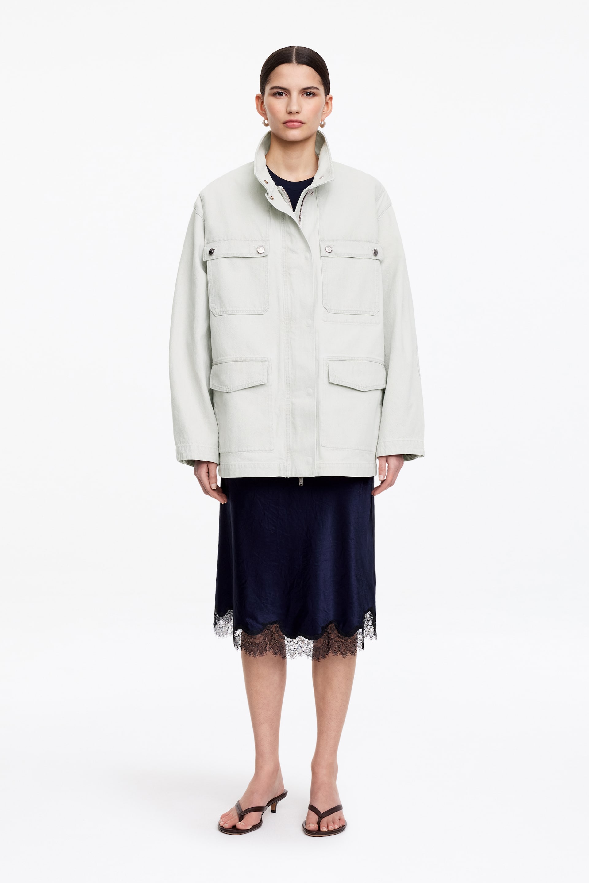Agrandir l'image: Une veste utilitaire gris clair est présentée de face, avec un col montant et une patte de boutonnage à pression dissimulée sur une fermeture éclair. Elle affiche quatre poches à rabat sur le devant, avec deux à la poitrine et deux à la taille, et une coupe décontractée.
