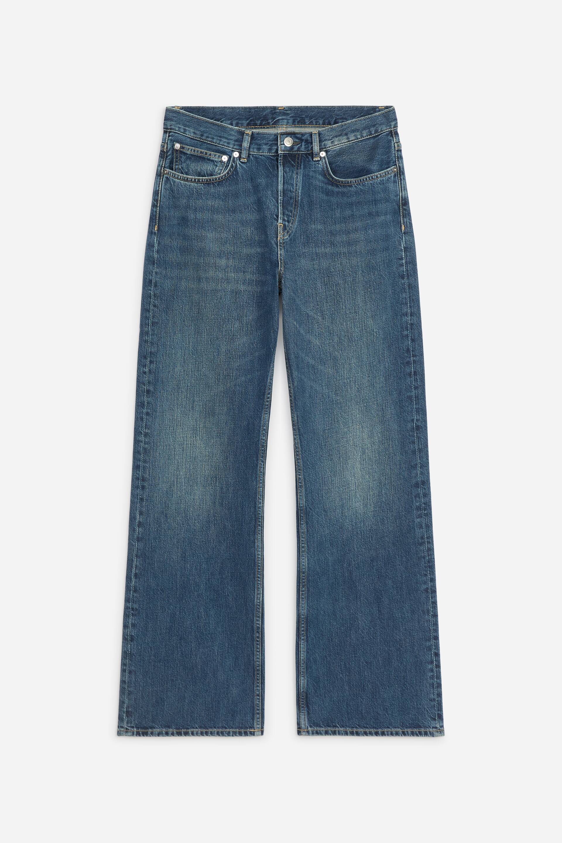 Ver imagem maior: Estes jeans de ganga azul de lavagem média estão virados para a frente, exibindo cintura de altura média com presilhas para cinto, um design clássico de cinco bolsos e fecho de braguilha com botões. As pernas de corte regular apresentam um desbotamento subtil nas coxas e prolongam-se numa silhueta boot-cut.