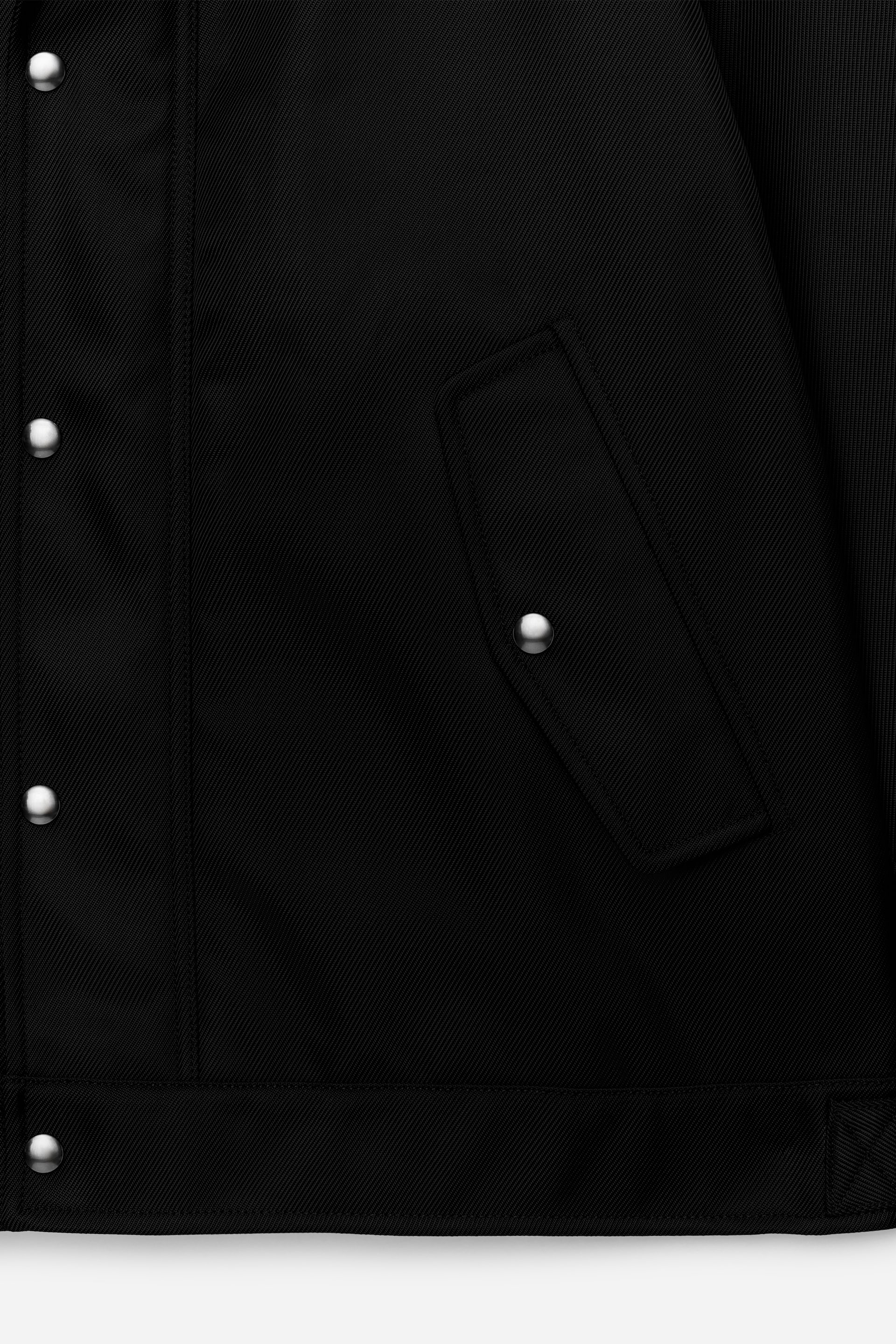 Agrandir l'image: Une veste noire présente une patte de boutonnage avant avec plusieurs boutons-pression argentés et une poche à rabat sécurisée par un seul bouton-pression argenté. La veste est dotée d'un tissage sergé diagonal subtil et d'une bande d'ourlet visible en bas.