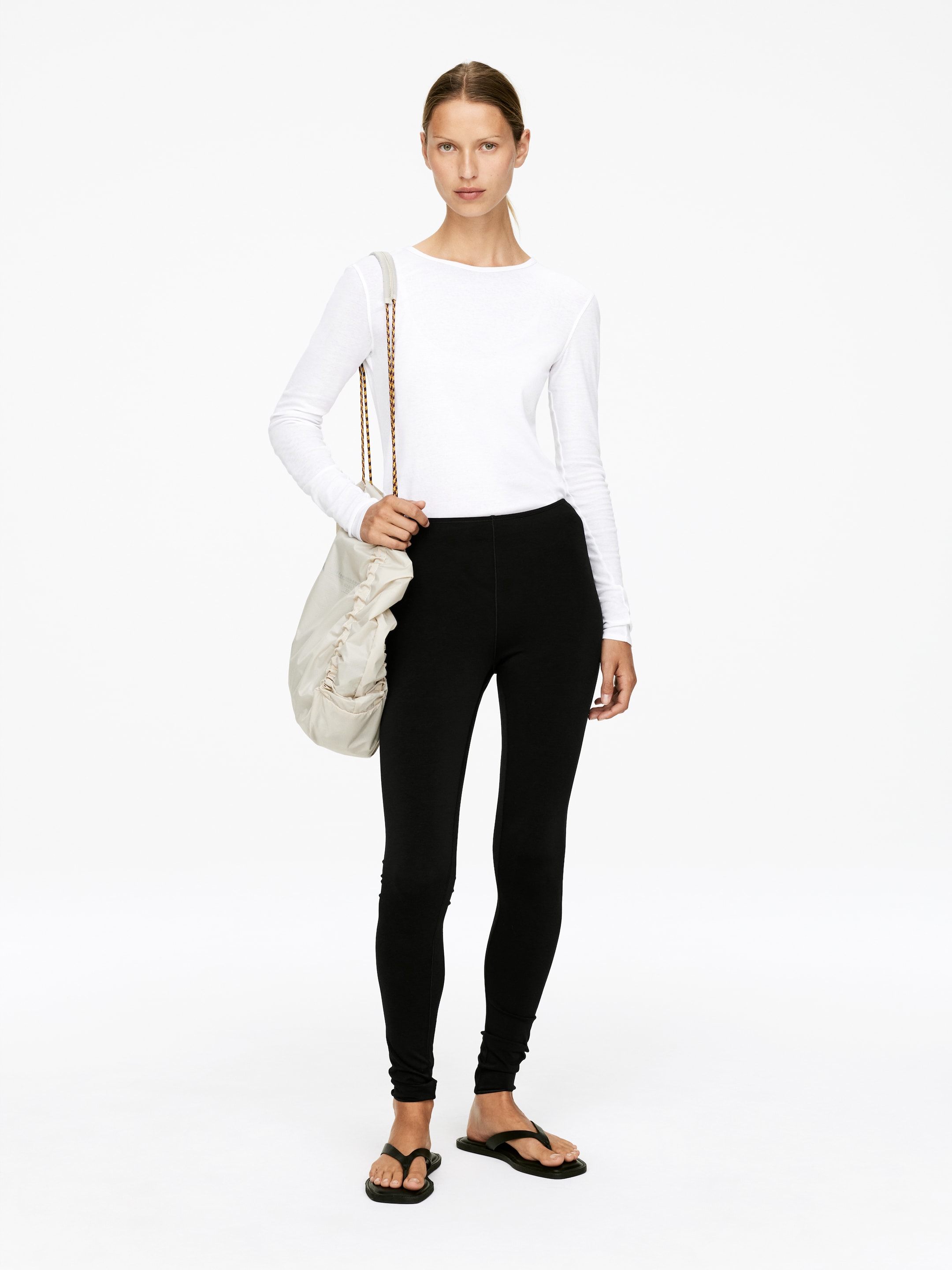 Visualizza immagine più grande: Un top bianco a maniche lunghe e leggings neri sono esposti su una modella rivolta in avanti. Il top presenta un girocollo e una vestibilità aderente, mentre i leggings mostrano una silhouette a lunghezza intera e aderente.