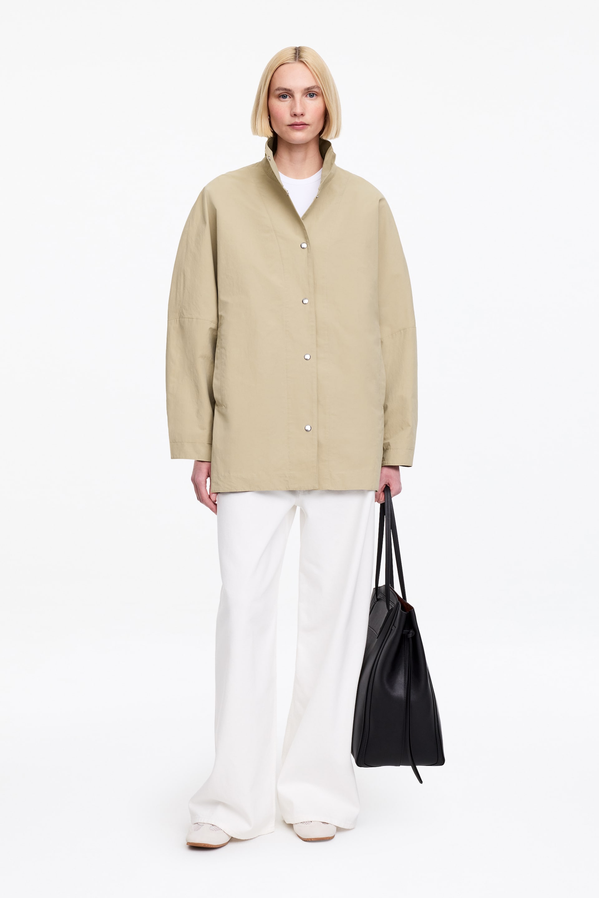 Visa större bild: En överdimensionerad beige skaljacka bärs av modellen. Den har en ståkrage och rena tryckknappsstängningar längs framsidan, lager på lager över en vit t-shirt.