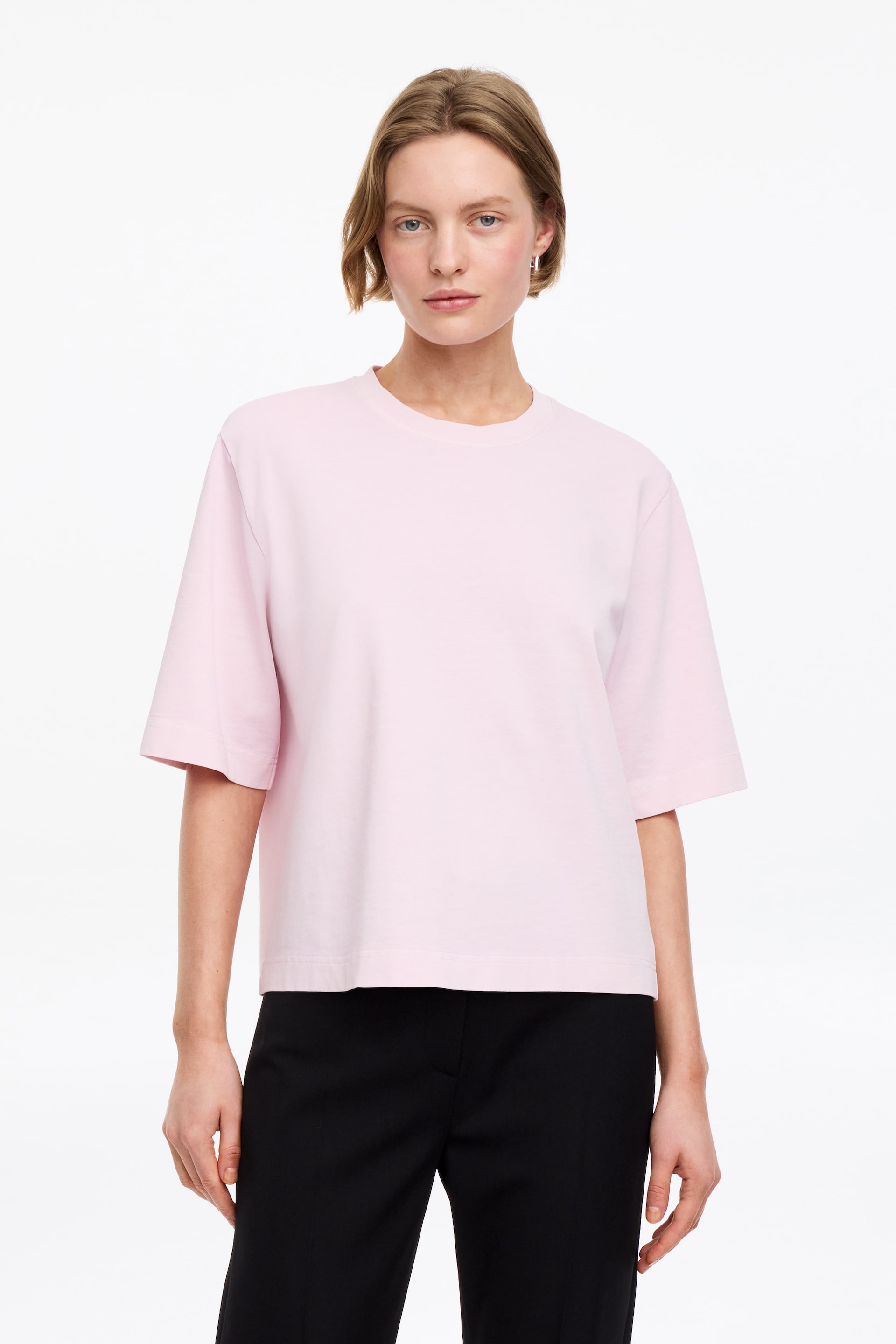 Visa större bild: Den ljusrosa t-shirten har en rund halsringning, vida ärmar i armbågslängd med vikta fållar och en rak nederkant. Den har en avslappnad, boxig passform när den visas framifrån.