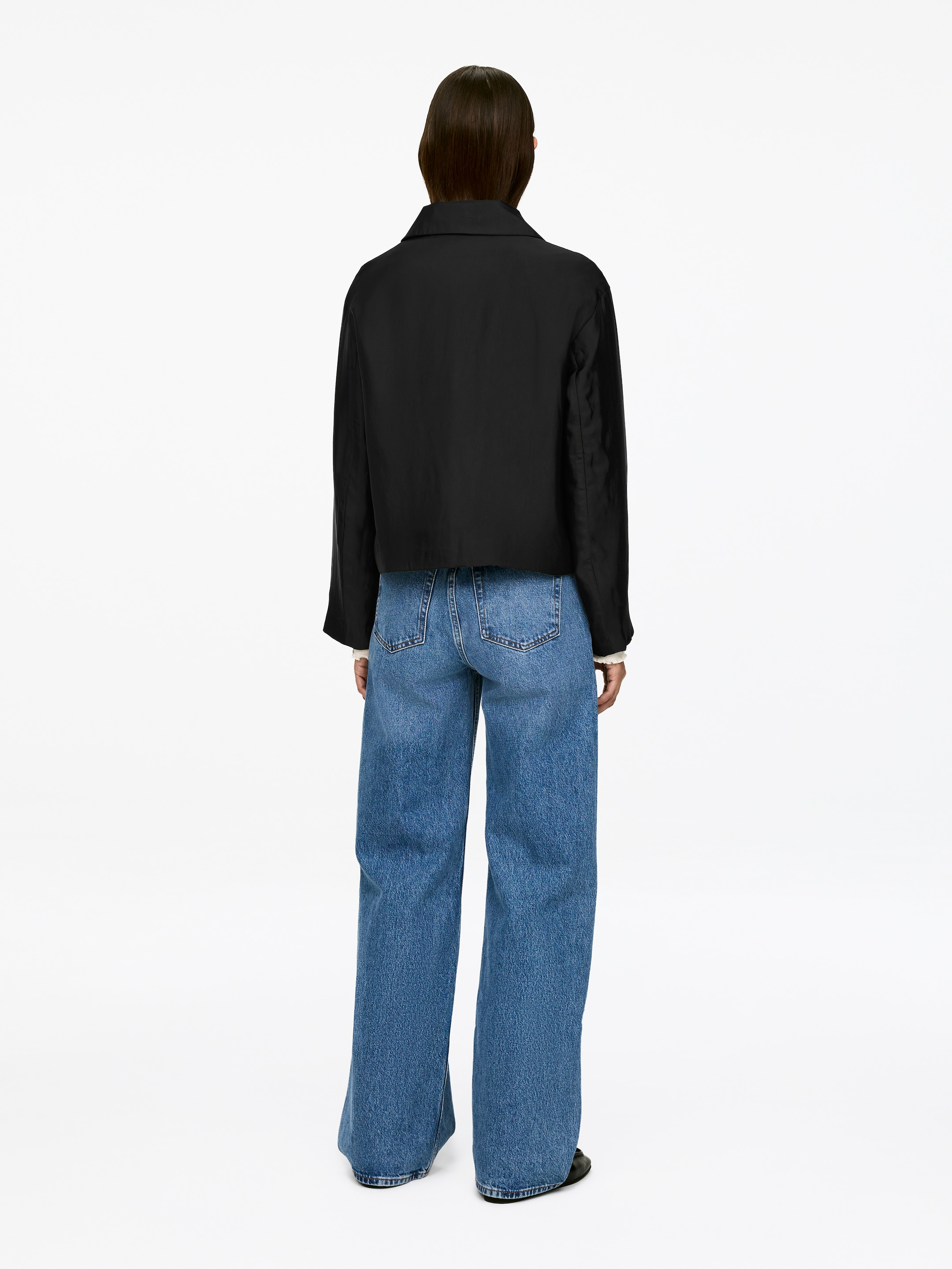 Größeres Bild ansehen: Ein schwarzes Overshirt mit Kragen und regulärer Passform wird vom Model getragen, das zudem blaue Jeans und ein weißes Kleidungsstück darunter trägt.