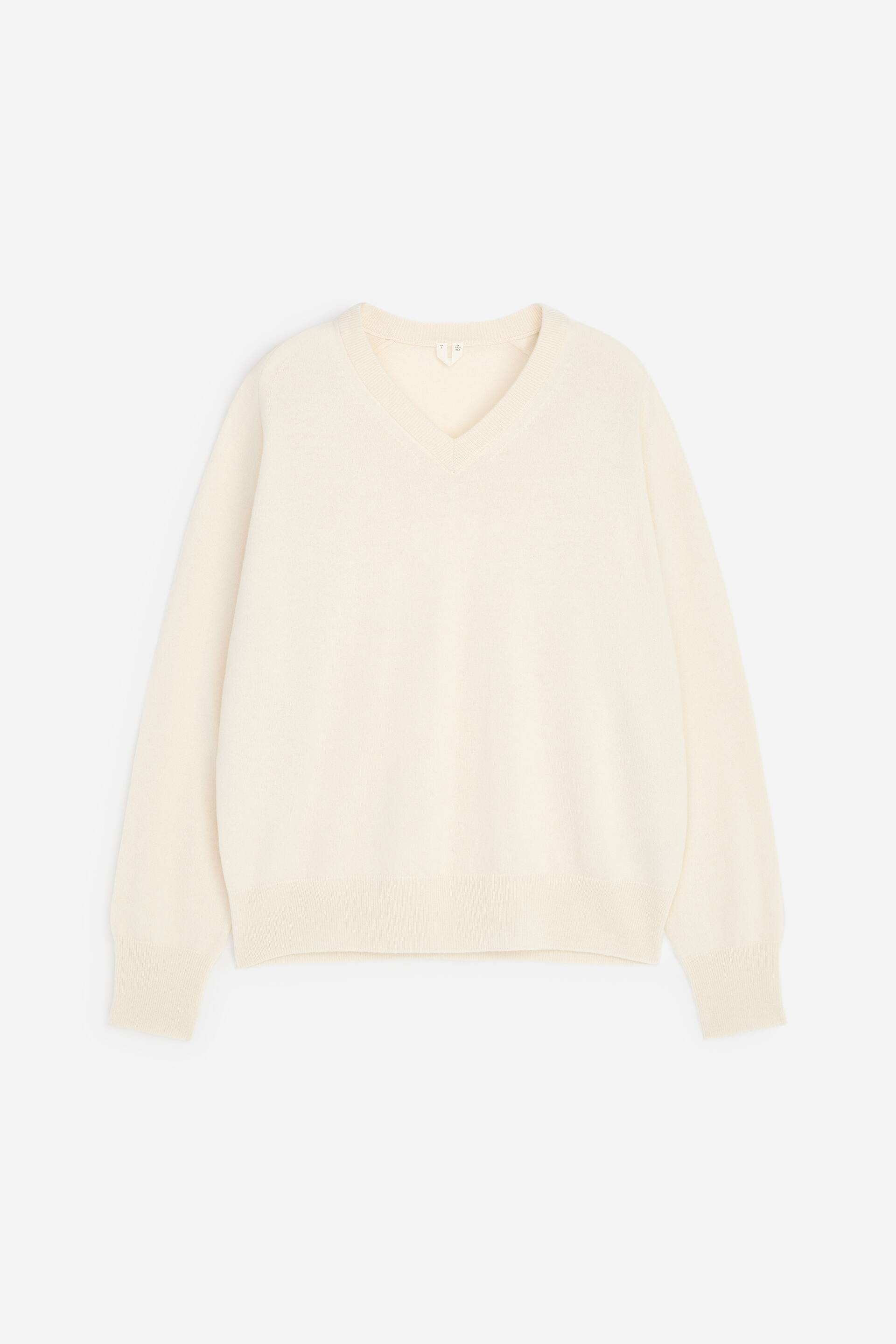 Ver imagen más grande: Un jersey de cuello en V de color crema muestra su parte delantera, con mangas largas que presentan puños acanalados y un dobladillo acanalado.