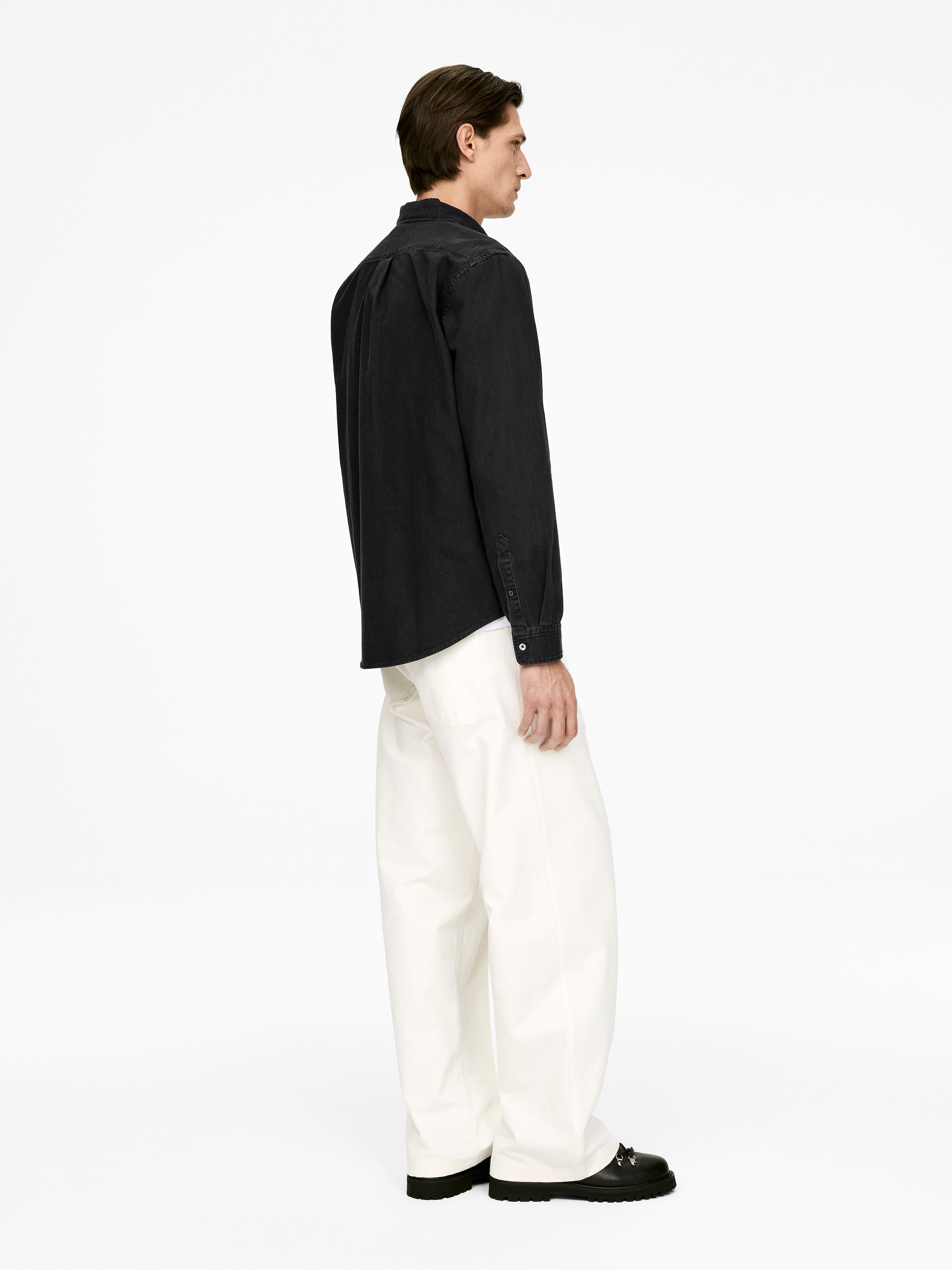 Agrandir l'image: Une chemise foncée à manches longues et à boutons, avec un col en pointe, un empiècement au dos et des poignets boutonnés, est portée. Elle est associée à un pantalon ample à jambes larges de couleur blanc cassé, avec l'ensemble visible de côté et légèrement de dos.