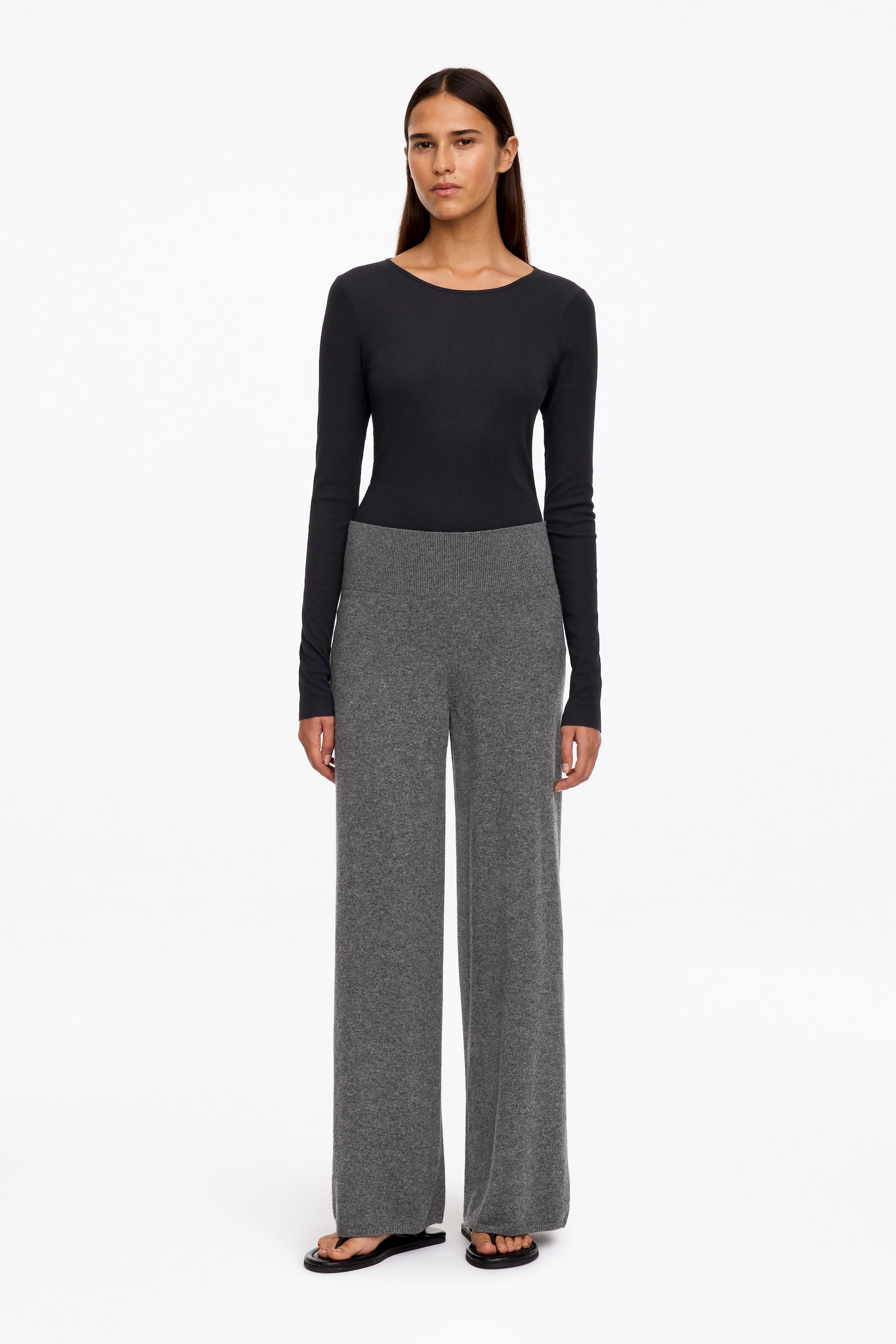 Agrandir l'image: Le mannequin porte un pantalon large en maille grise doté d’une large taille haute. Le pantalon est associé à un top noir ajusté à manches longues et à des sandales noires.