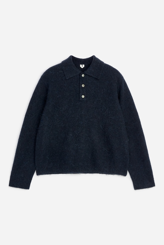Ein dunkelmarineblauer Strick-Polopullover ist von vorne zu sehen und zeichnet sich durch eine flauschige, gebürstete Textur sowie einen klassischen Kragen aus. Der Pullover verfügt über eine Knopfleiste mit drei hellen Knöpfen, lange Ãrmel und einen geraden Saum. - 1