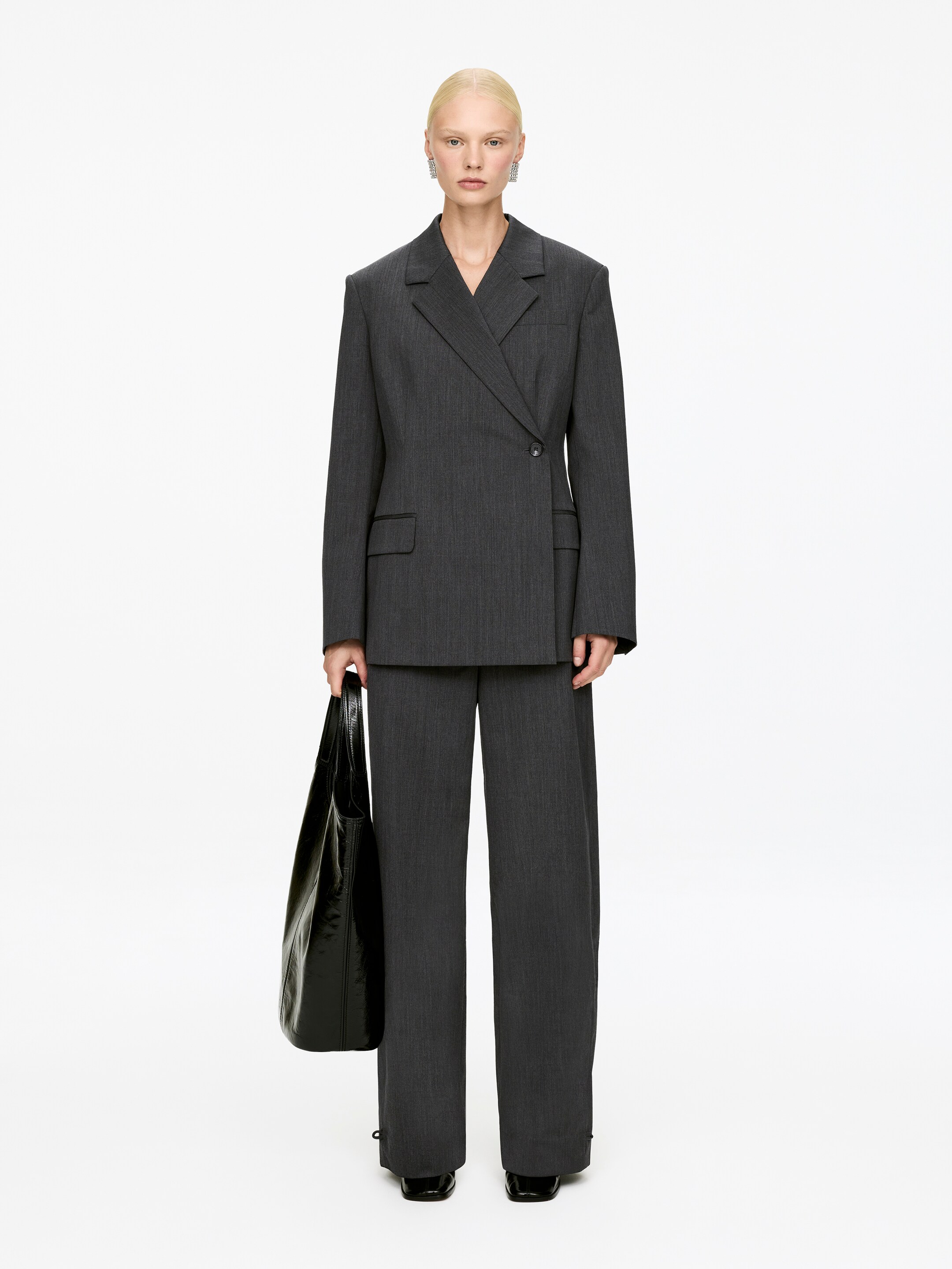 Agrandir l'image: Un costume-pantalon à rayures anthracite est présenté, face vers l'avant. Le blazer croisé présente des revers crantés, des épaules structurées et rembourrées, et des poches à rabat, tandis que le pantalon à jambes larges complète la silhouette du costume.