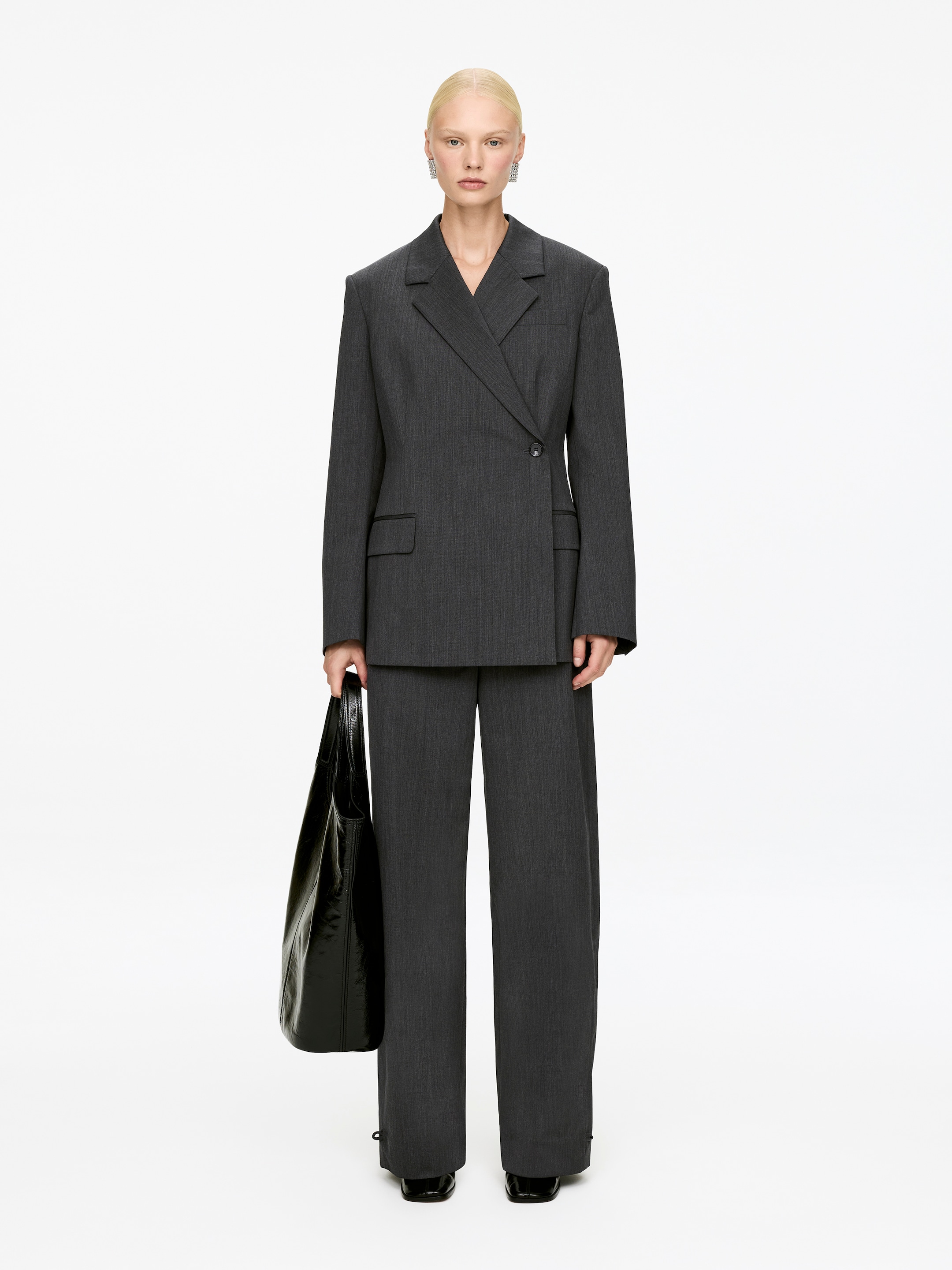 Visualizza immagine più grande: Un completo pantalone gessato grigio scuro viene presentato, rivolto in avanti. Il blazer doppiopetto presenta revers a tacche, spalle strutturate imbottite e tasche con patta, mentre i pantaloni a gamba larga completano il profilo del completo.