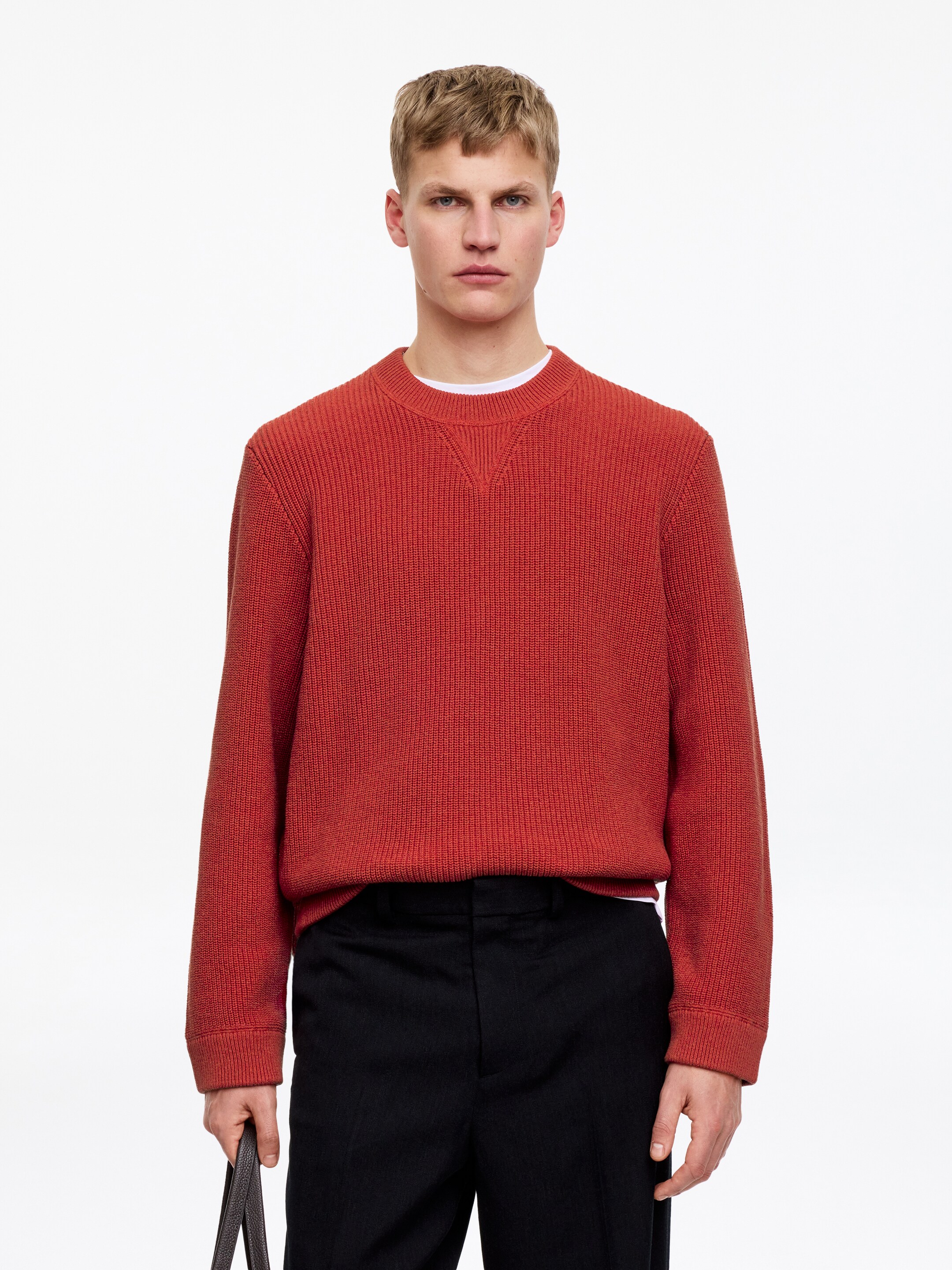Ver imagen más grande: La modelo lleva un jersey texturado de color naranja rojizo, tejido en punto half-cardigan, con cuello redondo, puños y bajo en canalé. Este jersey de corte regular se lleva sobre una camiseta interior blanca y se combina con pantalones negros.