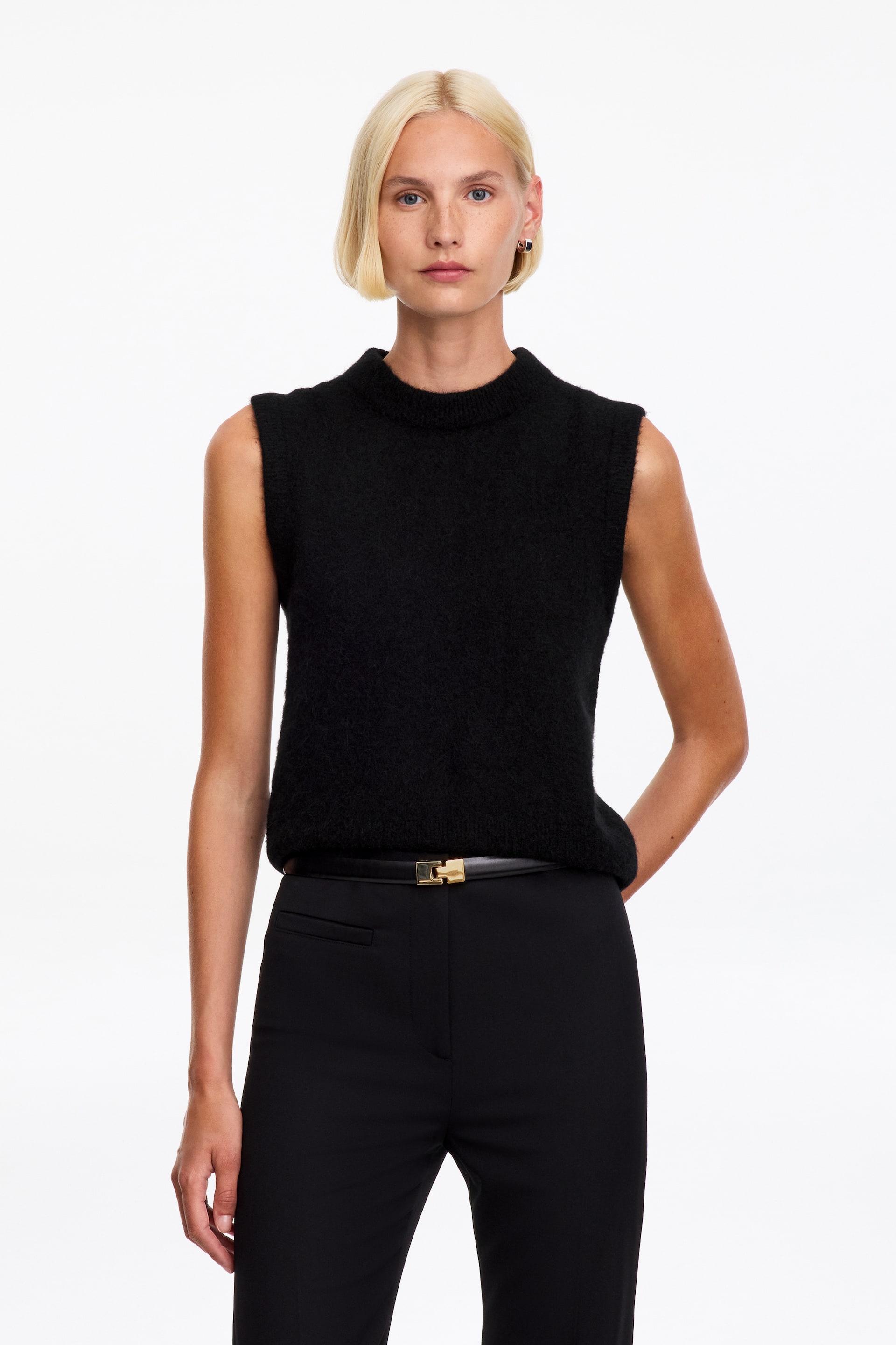 Visualizza l'immagine ingrandita: Il modello indossa un gilet nero in maglia testurizzata con girocollo a coste e design senza maniche. Il gilet è abbinato a pantaloni neri e a una cintura nera con fibbia dorata.