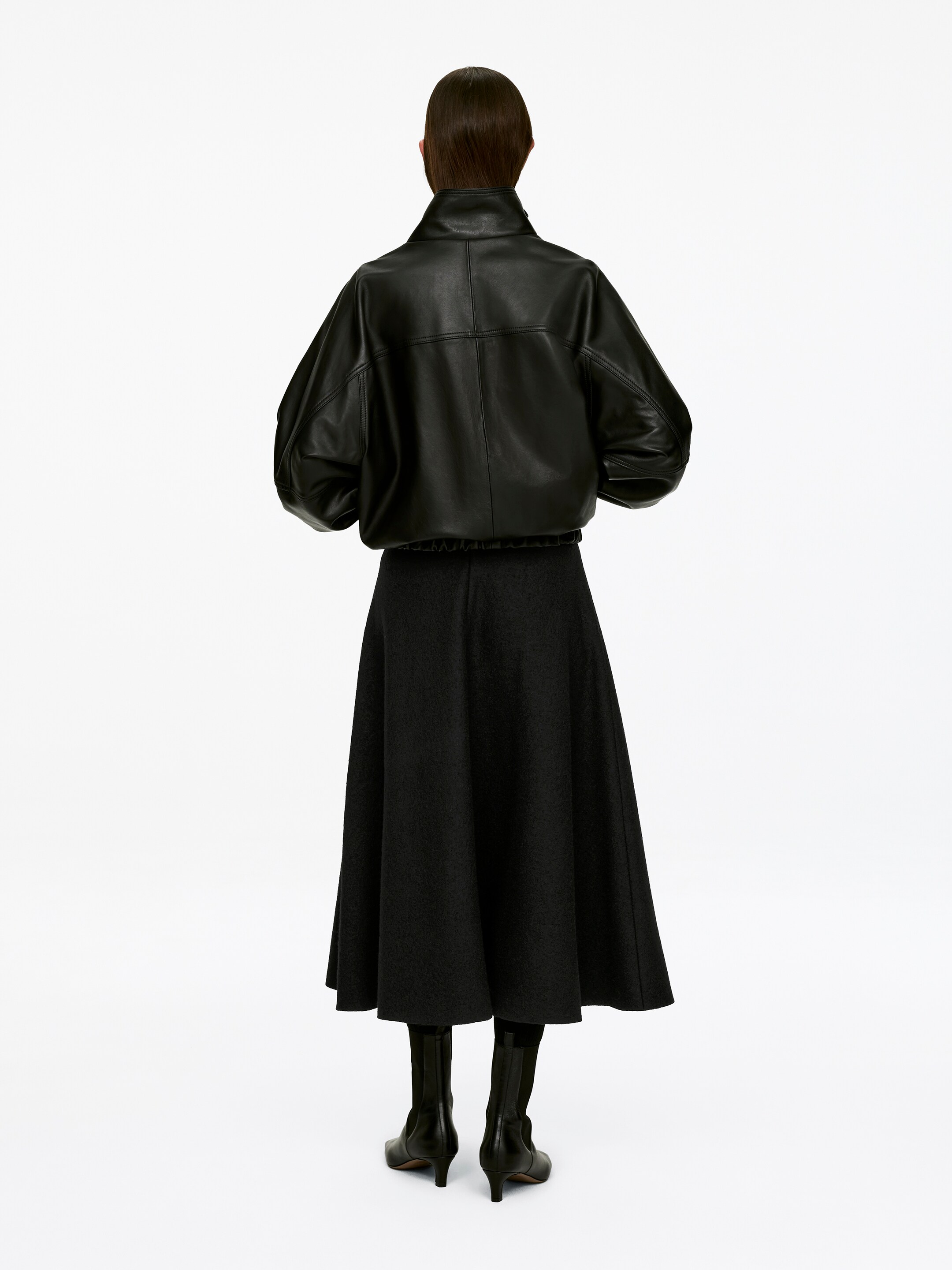 Agrandir l'image: Une jupe en laine à cercle complet de style longueur cheville est portée par le mannequin, superposée d'une veste en cuir noir et stylisée avec des bottes noires.