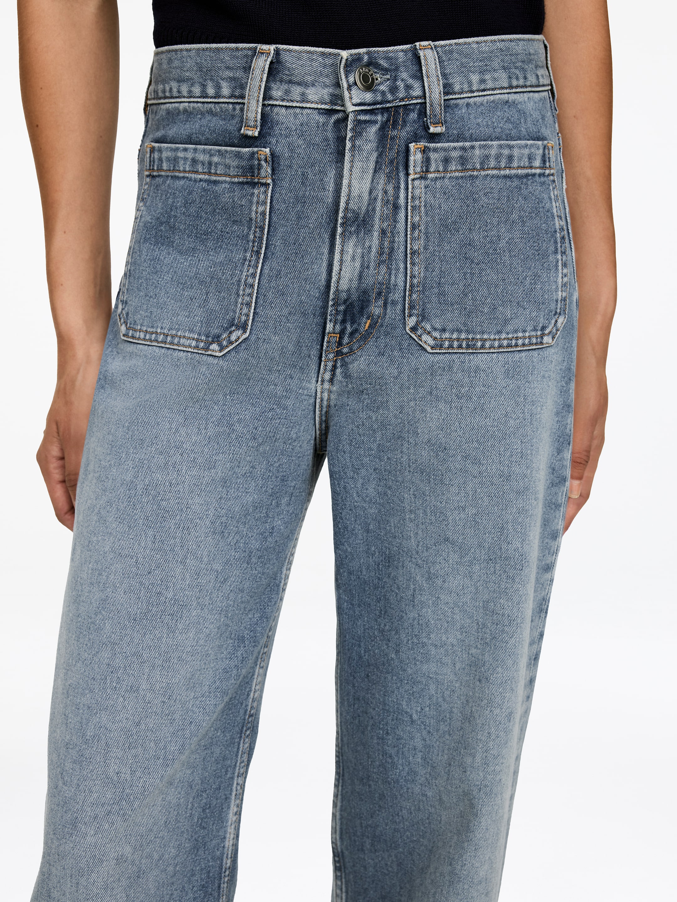 Visualizza immagine più grande: Jeans in denim chiaro vengono indossati dalla modella, con vita alta, chiusura con bottoni e cerniera e due grandi tasche rettangolari applicate sul davanti. Un top scuro è indossato infilato nella vita dei jeans.